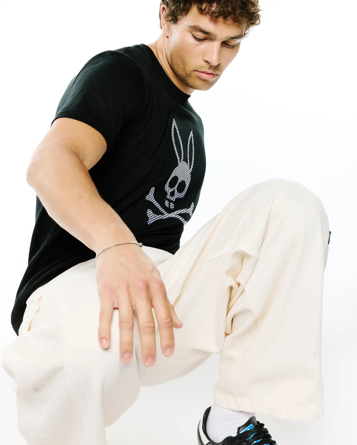 Mens Stan Graphic Tee, a black classic fit soft jersey t-shirt featuring a prominent white and black checkered Psycho Bunny skull logo graphic on the chest, embodying refined streetwear.