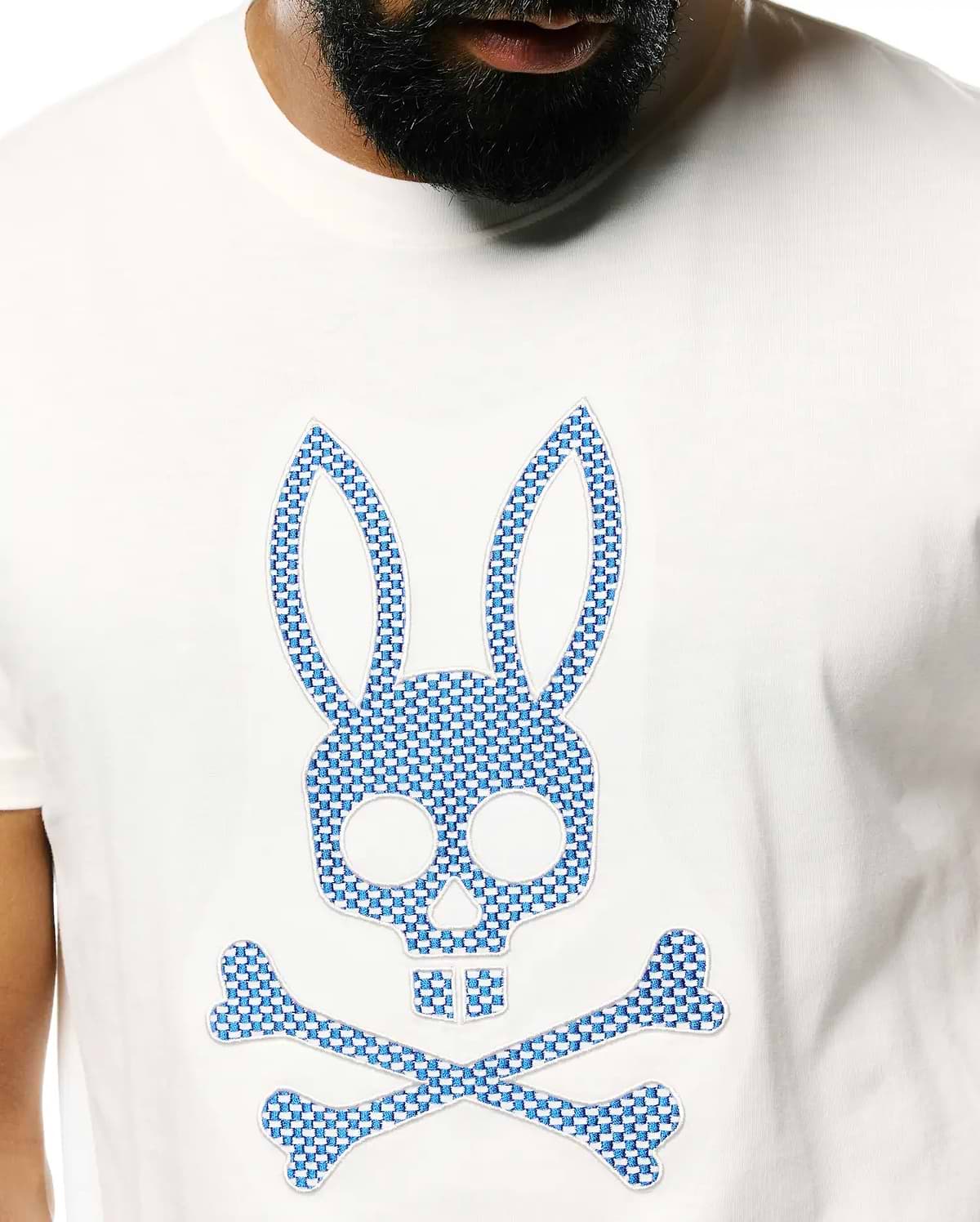 Mens Stan Pima Cotton Graphic Tee, a classic fit white Pima cotton jersey t-shirt with a large central embroidered Psycho Bunny skull and crossbones logo featuring a blue and white checkered pattern.