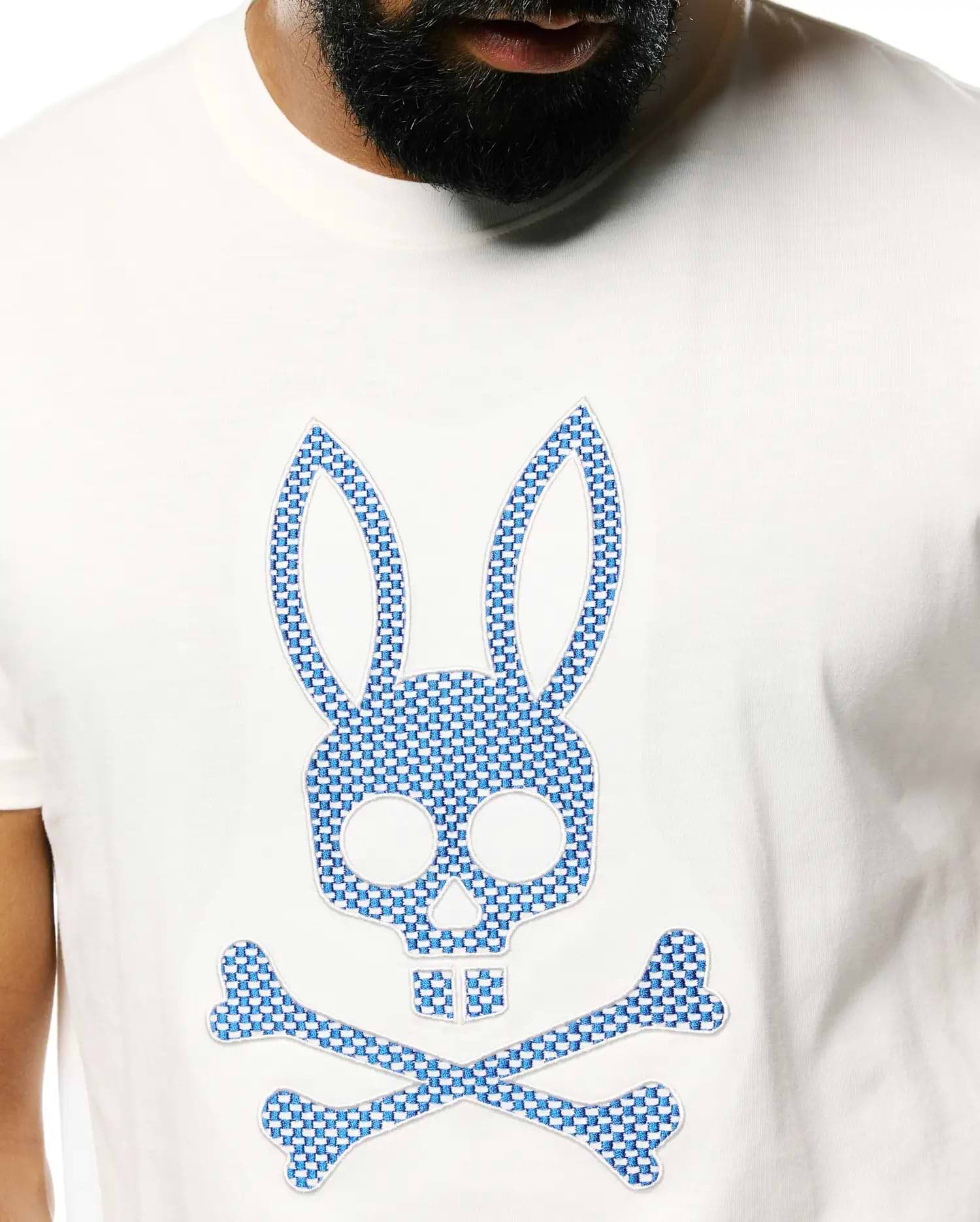 Mens Stan Pima Cotton Graphic Tee, a classic fit white Pima cotton jersey t-shirt with a large central embroidered Psycho Bunny skull and crossbones logo featuring a blue and white checkered pattern.
