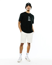 Mens Alex Relaxed Back Graphic Tee in black jersey, featuring a light blue outlined Psycho Bunny skull logo and white text on the left chest, paired with cream shorts, a black logo cap, and white sneakers.
