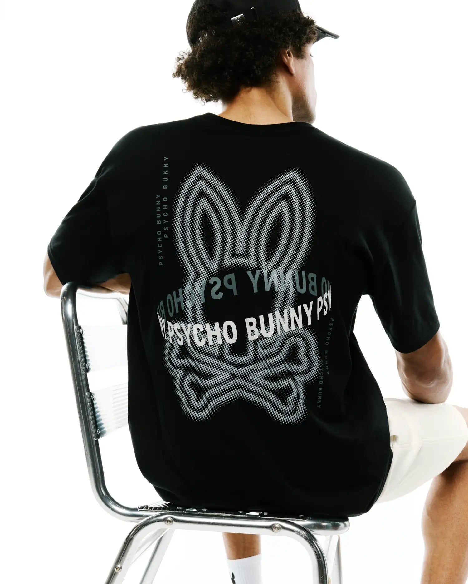 Mens Alex Relaxed Back Graphic Tee in black jersey knit, featuring a large white and grey dotted Psycho Bunny skull graphic on the back and vertical Psycho Bunny text along the shoulders.