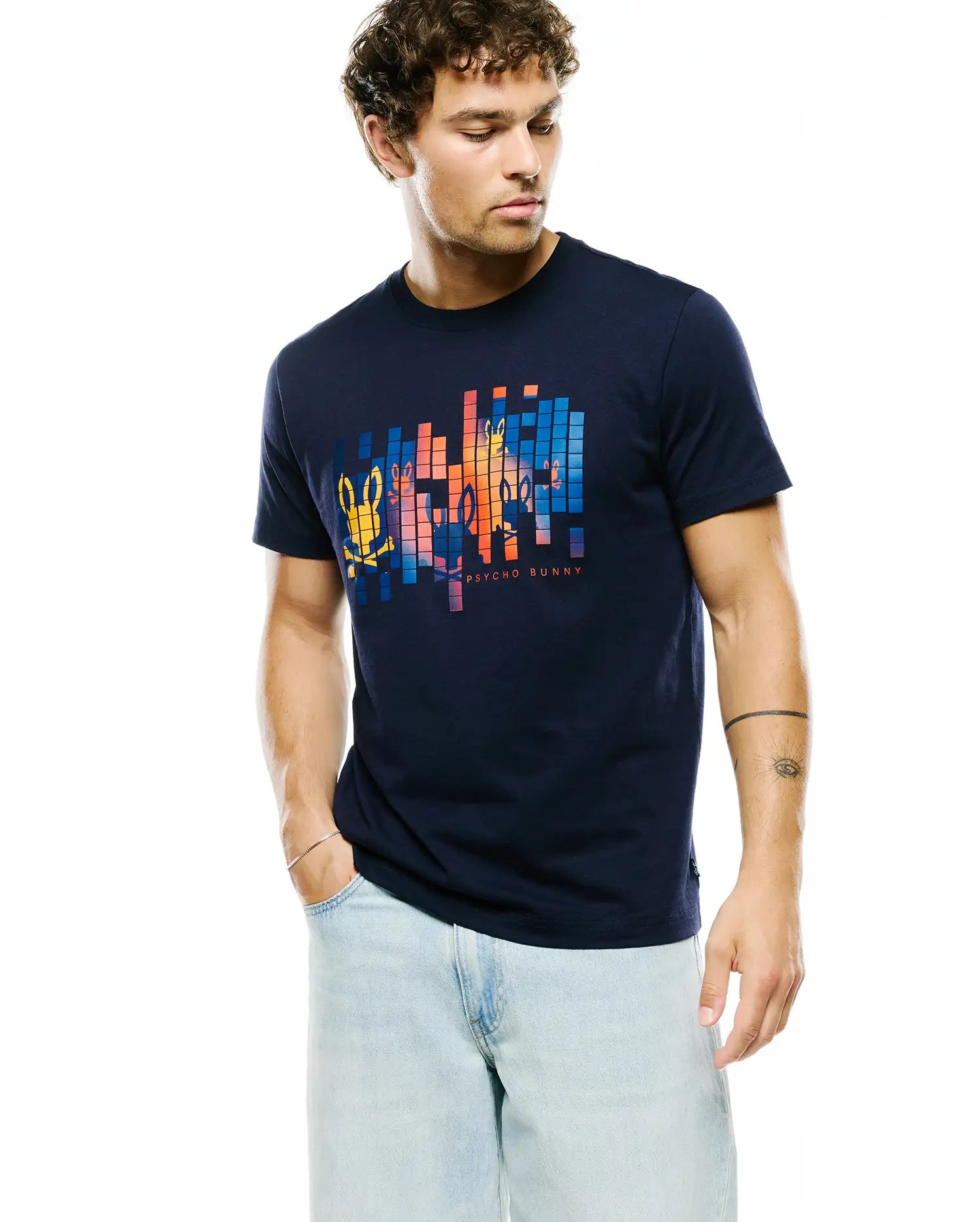 Mens Zander Graphic Tee, a navy blue classic fit jersey t-shirt featuring a large pixelated chest graphic with colorful Psycho Bunny skull logos and PSYCHO BUNNY text.