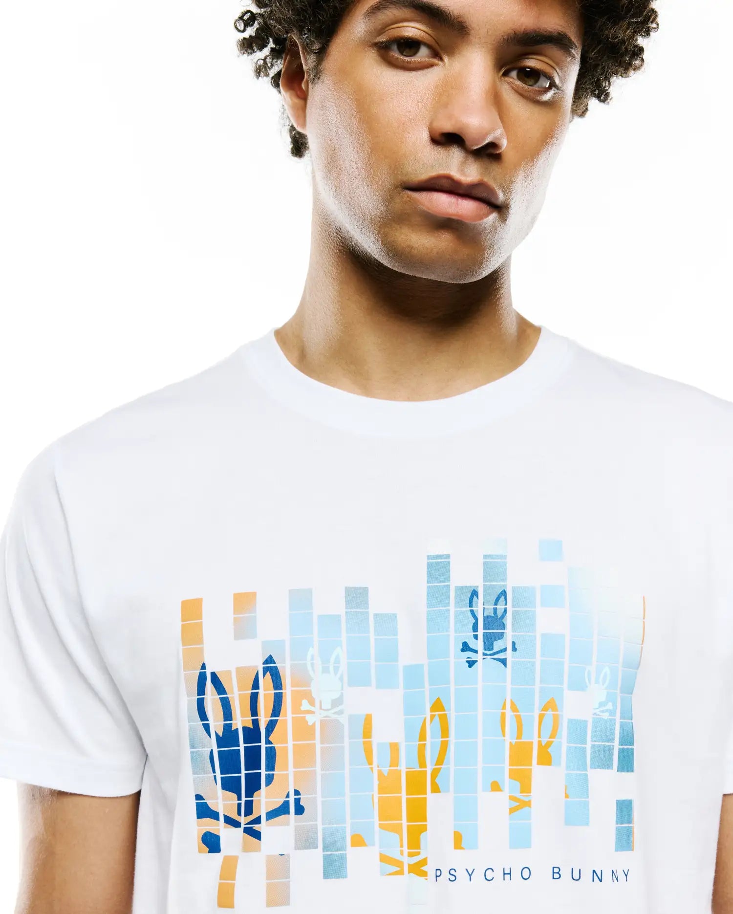 Mens Zander Graphic Tee, a white jersey t-shirt with a large chest graphic featuring pixelated blue, orange, and light blue Psycho Bunny skull logos and PSYCHO BUNNY text, classic fit.