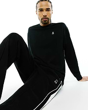 Black Mens Norman Long Sleeve Oversized Fit Tee with a white Psycho Bunny skull logo on the left chest, and black track pants with a white side stripe and a thigh bunny logo.