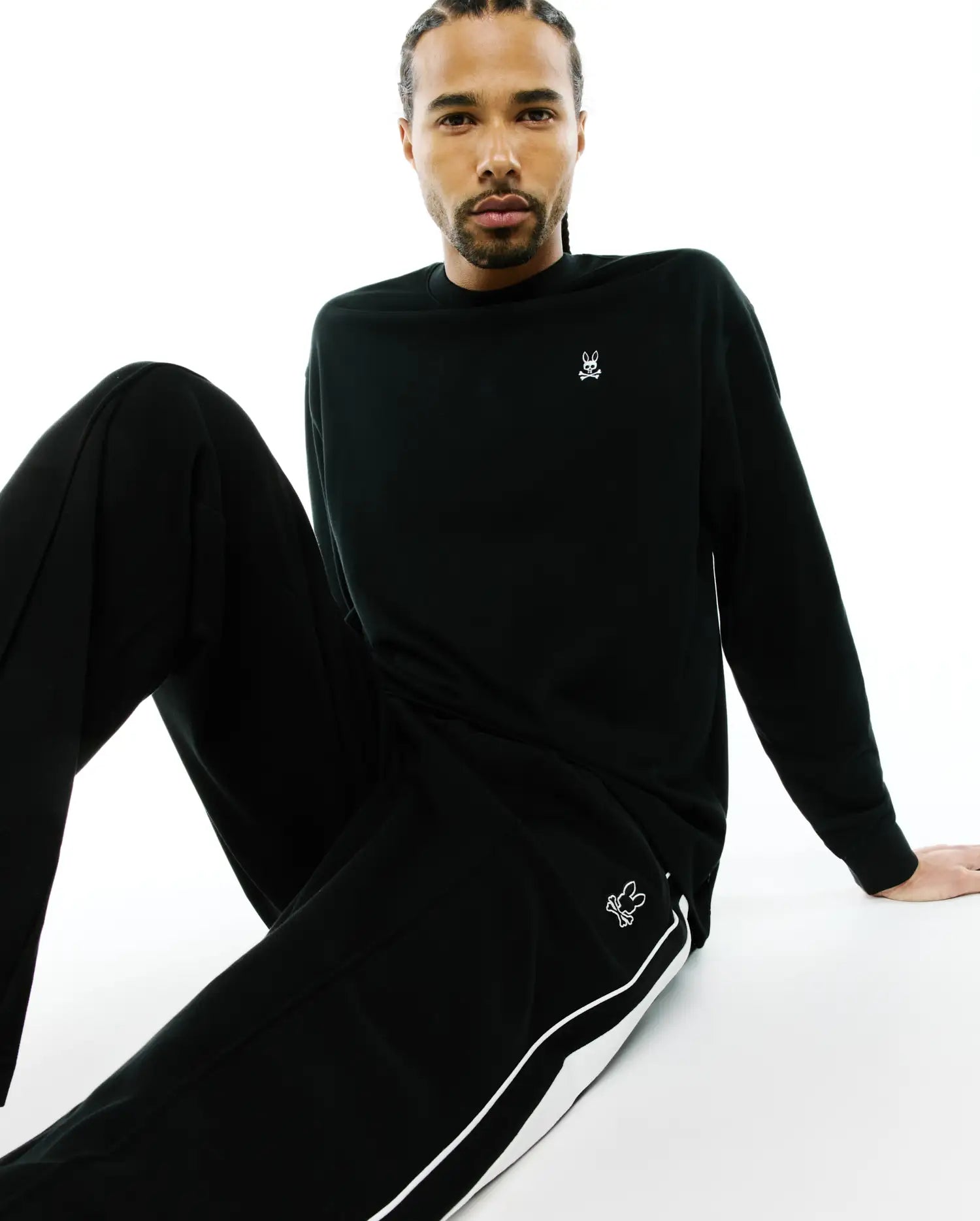 Black Mens Norman Long Sleeve Oversized Fit Tee with a white Psycho Bunny skull logo on the left chest, and black track pants with a white side stripe and a thigh bunny logo.