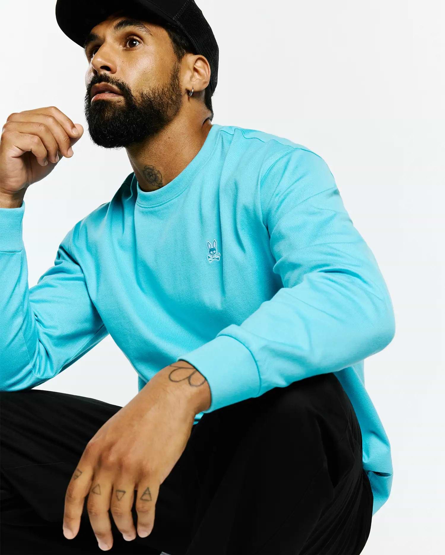 Mens Norman Long Sleeve Relaxed Fit Tee in vibrant aqua smooth jersey knit, featuring a small white embroidered Psycho Bunny skull logo on the left chest.