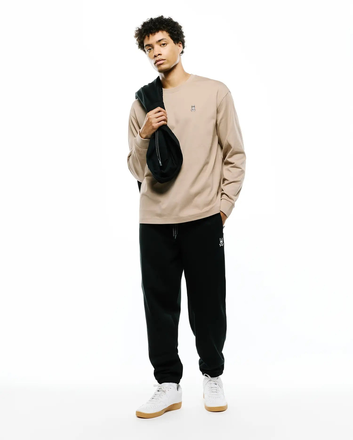 Beige Mens Norman Long Sleeve Relaxed Fit Tee with a small embroidered bunny skull left chest, paired with black relaxed fit sweatpants featuring a white bunny skull left thigh.