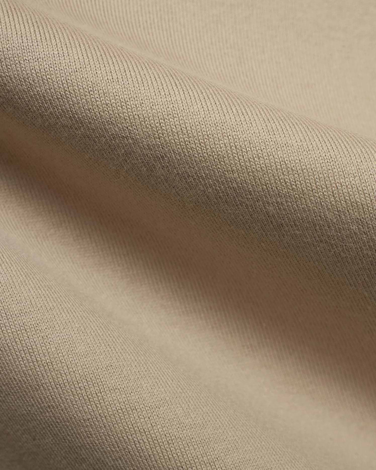 Mens Norman Long Sleeve Relaxed Fit Tee, crafted from a premium, soft beige jersey knit fabric, showcasing its refined texture and comfortable drape in a close-up detail.