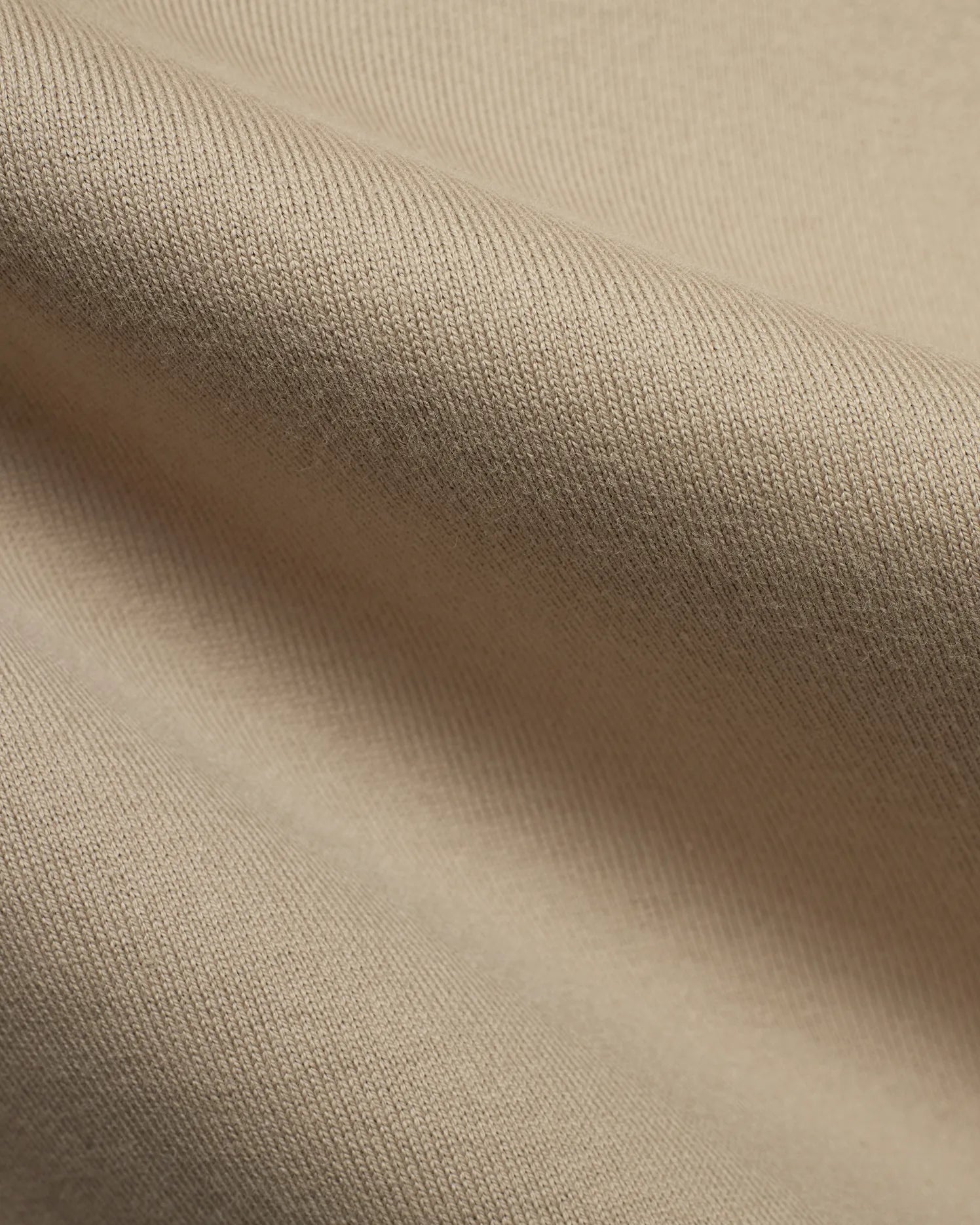 Mens Norman Long Sleeve Relaxed Fit Tee, crafted from a premium, soft beige jersey knit fabric, showcasing its refined texture and comfortable drape in a close-up detail.