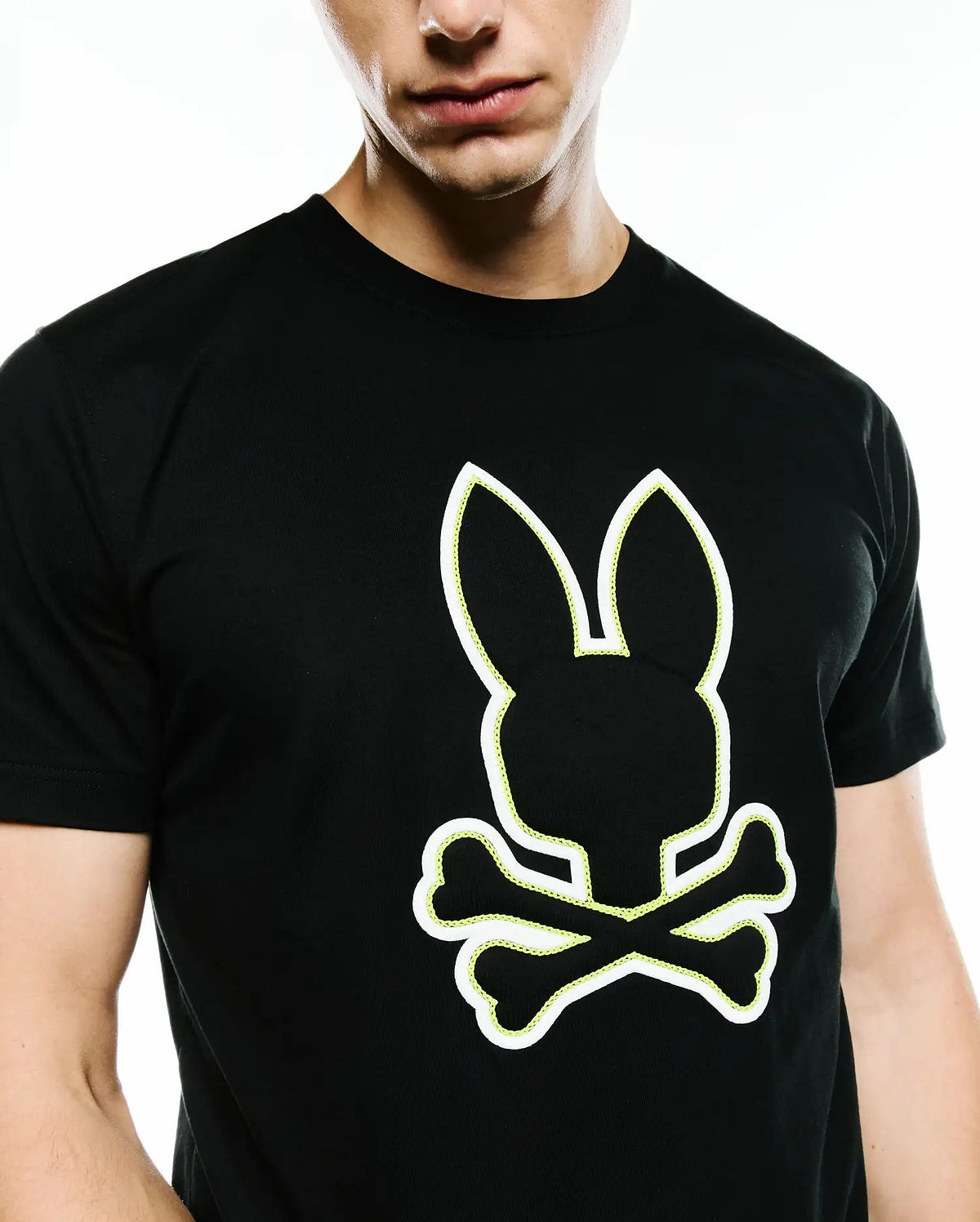 Mens Bruno Graphic Tee, a black classic fit jersey t-shirt featuring a prominent white outline Psycho Bunny skull logo with vibrant neon yellow stitching detail on the chest.