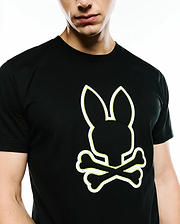 Mens Bruno Graphic Tee, a black classic fit jersey t-shirt featuring a prominent white outline Psycho Bunny skull logo with vibrant neon yellow stitching detail on the chest.
