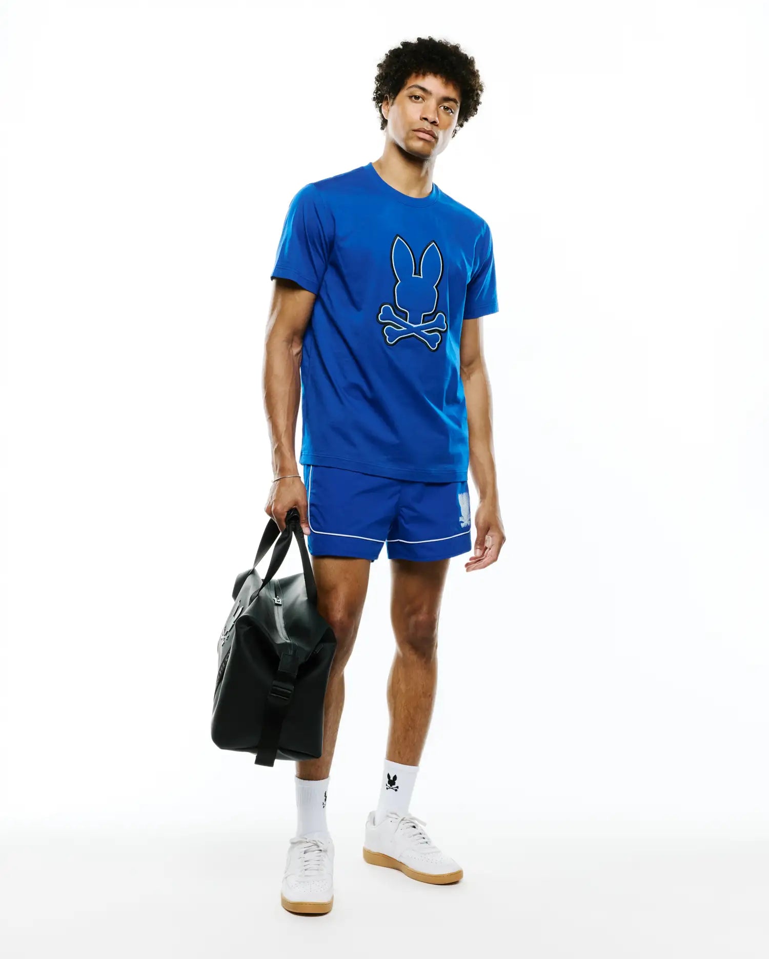 Mens Bruno Graphic Tee, a royal blue jersey t-shirt with a large white-outlined Psycho Bunny skull logo on the chest, complemented by royal blue athletic shorts with white piping and a small bunny logo, plus white logo socks.
