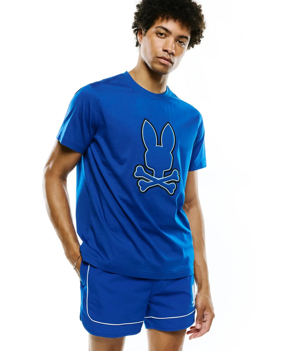 Royal blue Mens Bruno Graphic Tee, a classic fit jersey knit t-shirt featuring a large, centered white Psycho Bunny skull and crossbones graphic with a black outline.