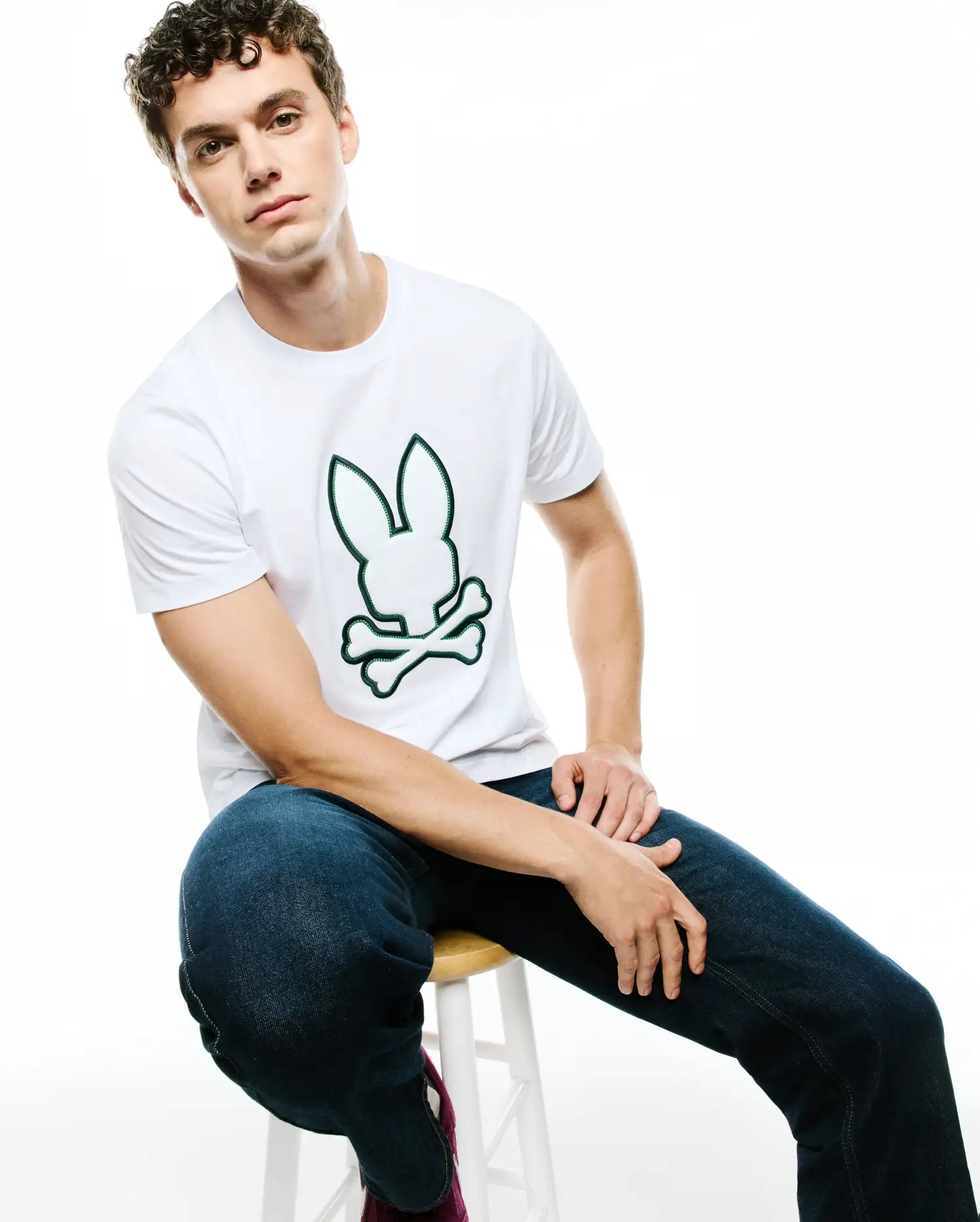 Mens Bruno Graphic Tee, white classic fit jersey t-shirt featuring a large, centered green-outlined Psycho Bunny skull and crossbones graphic logo.