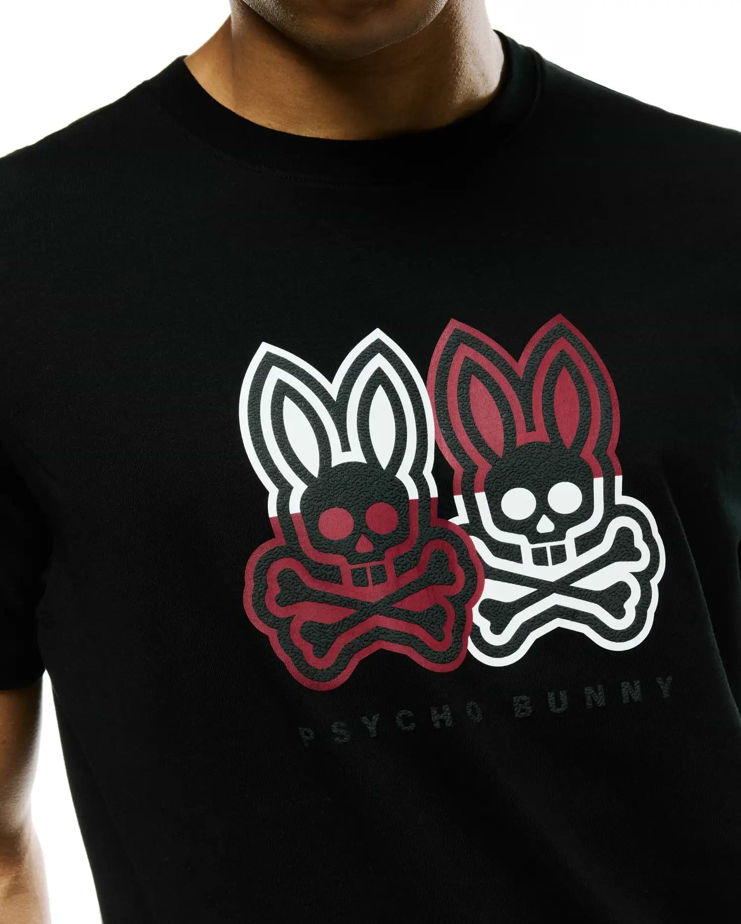 Mens Ledger Graphic Tee, a black jersey knit t-shirt with a classic fit, featuring a large textured chest graphic of two Psycho Bunny skull logos, one red and black, one white and black, with Psycho Bunny text below.
