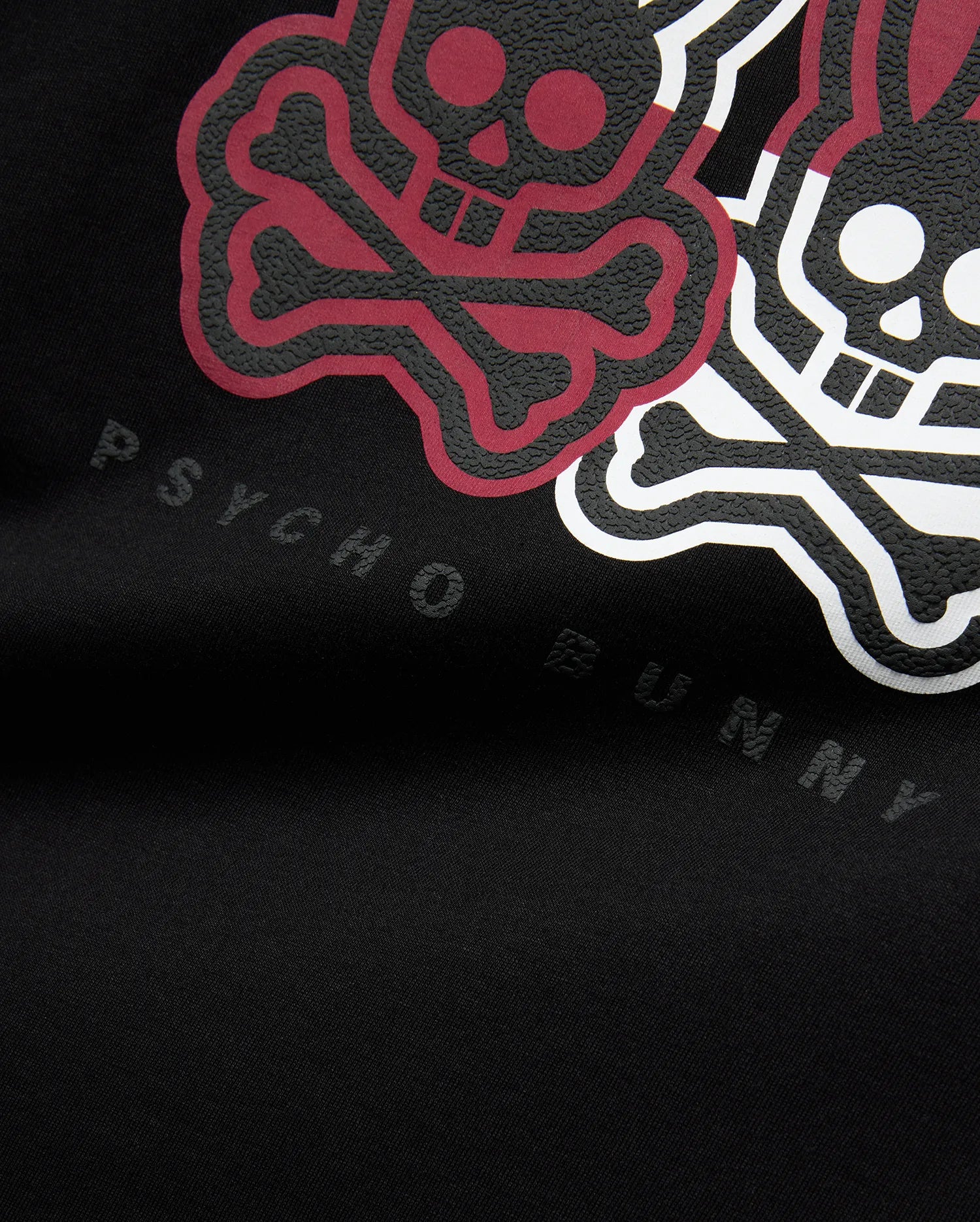 Mens Ledger Graphic Tee in black jersey knit, featuring a large, raised, textured graphic of maroon and white bunny skulls and crossbones, with subtle embossed Psycho Bunny text below.