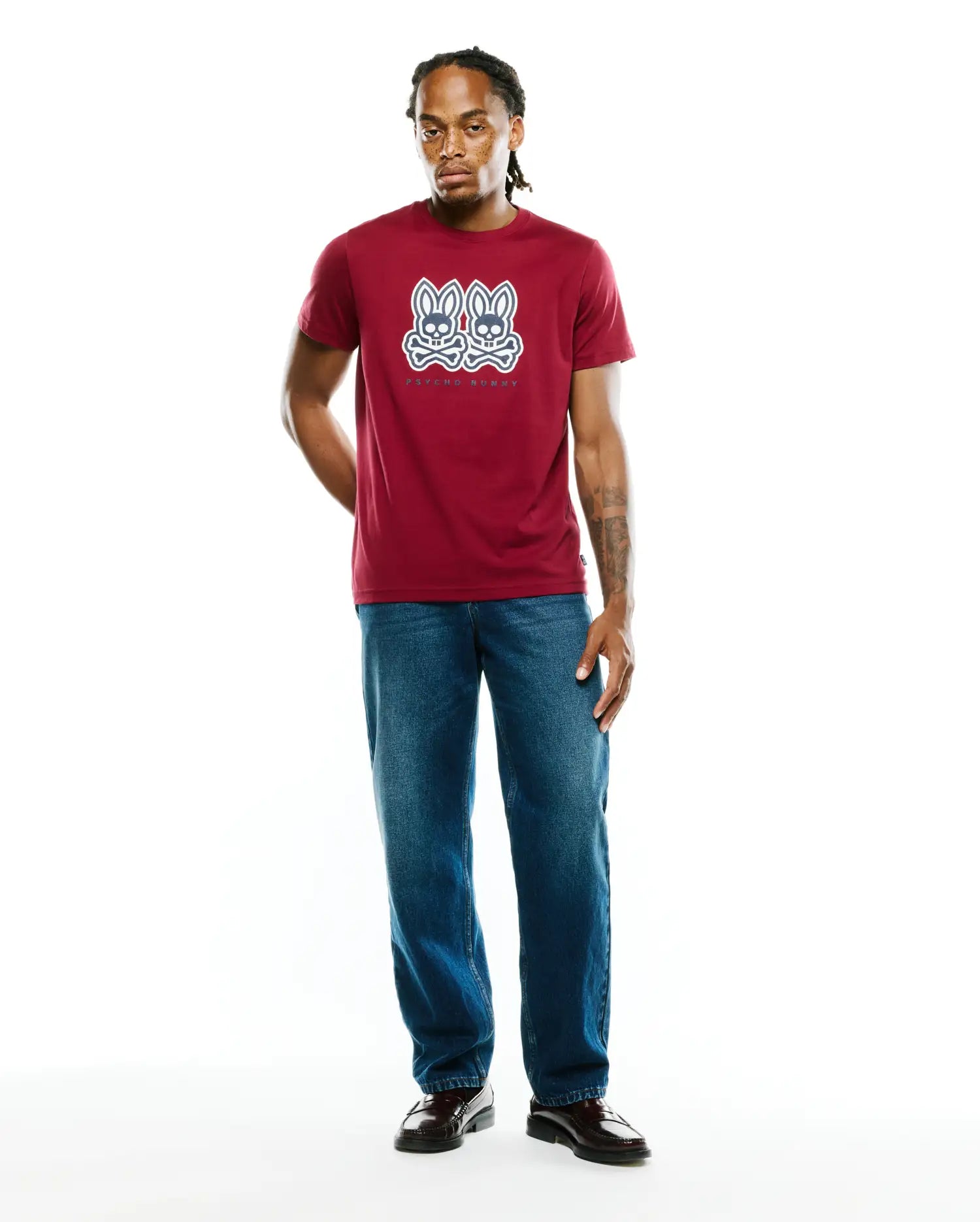 Mens Ledger Graphic Tee, a maroon classic fit soft jersey t-shirt featuring a large white and navy double Psycho Bunny skull and crossbones graphic with text on the chest.
