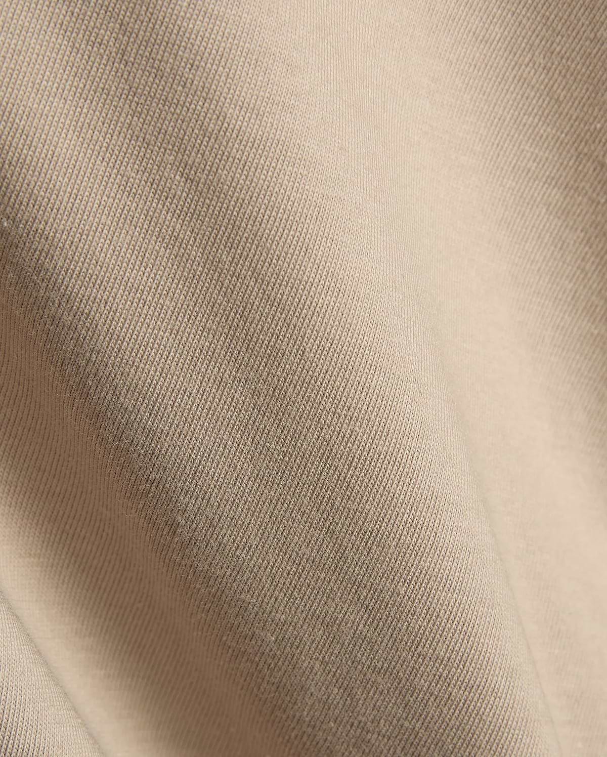 Psycho Bunny Mens Conan Back Graphic Tee in a warm, light beige, showcasing the refined, soft diagonal ribbed knit jersey fabric texture, characteristic of premium streetwear.