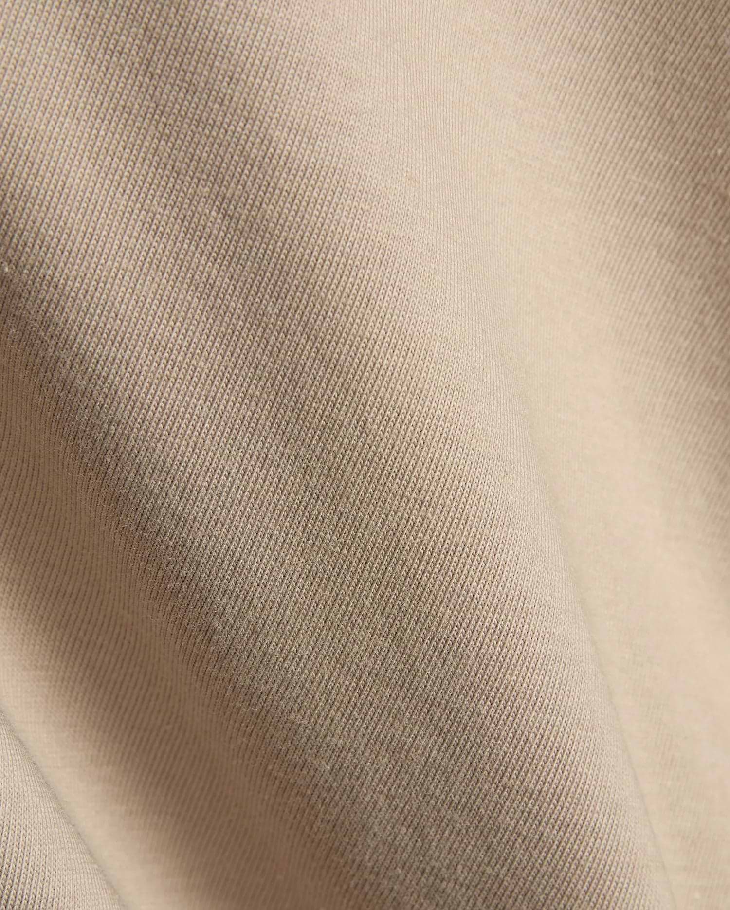 Psycho Bunny Mens Conan Back Graphic Tee in a warm, light beige, showcasing the refined, soft diagonal ribbed knit jersey fabric texture, characteristic of premium streetwear.
