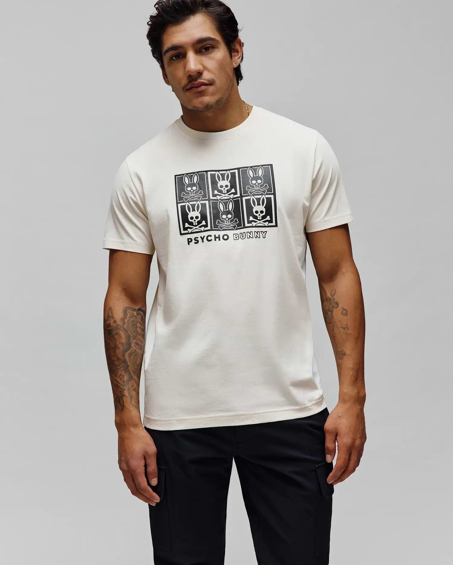 Mens Keon Graphic Tee, a cream classic fit jersey t-shirt with a large black central graphic print featuring six Psycho Bunny skull and crossbones logos and PSYCHO BUNNY text.