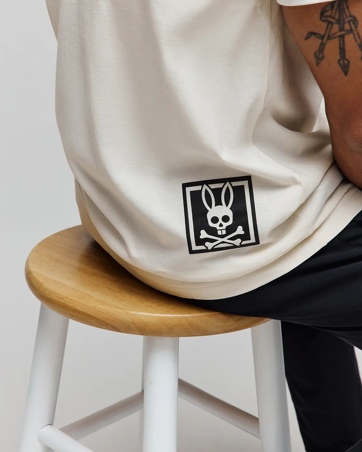 Mens Keon Graphic Tee in cream, featuring a relaxed fit and smooth jersey knit. A large black Psycho Bunny skull and crossbones logo graphic is printed on the lower back, framed by a square.