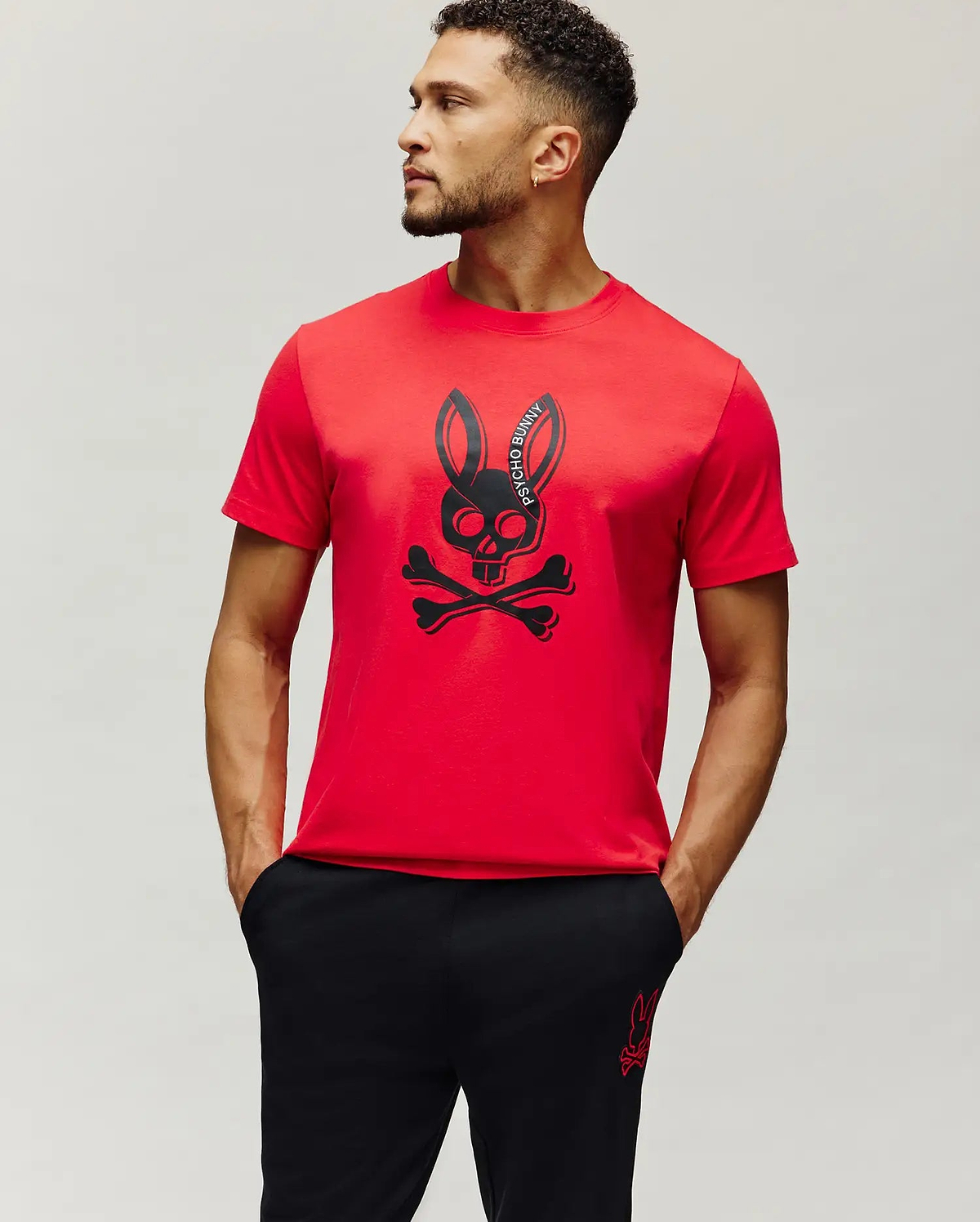 Mens Serge Embroidered Bunny Graphic Tee in vibrant red, featuring a large central black Psycho Bunny skull and crossbones graphic print with curved brand text, on a classic fit smooth jersey knit.