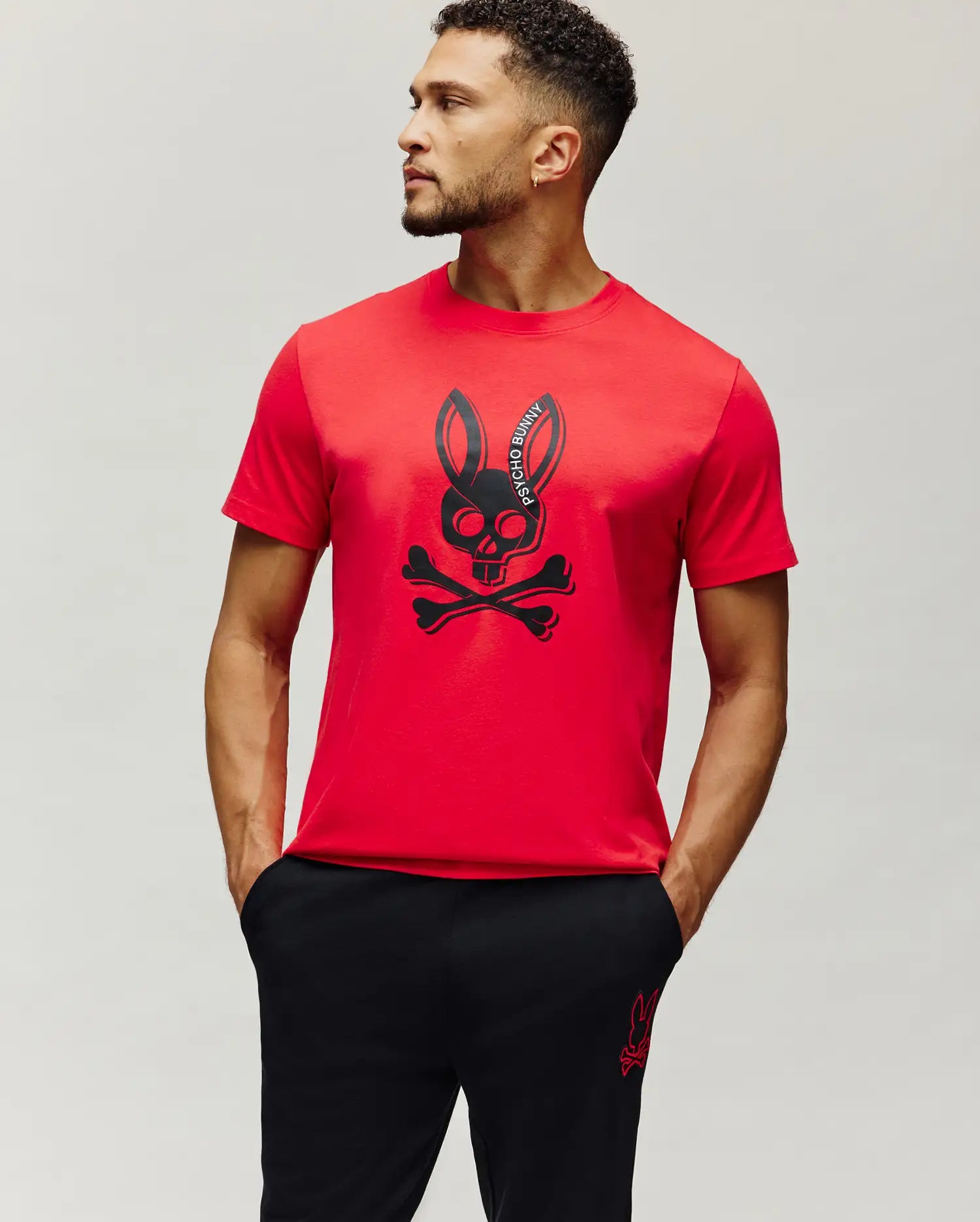 Mens Serge Embroidered Bunny Graphic Tee in vibrant red, featuring a large central black Psycho Bunny skull and crossbones graphic print with curved brand text, on a classic fit smooth jersey knit.