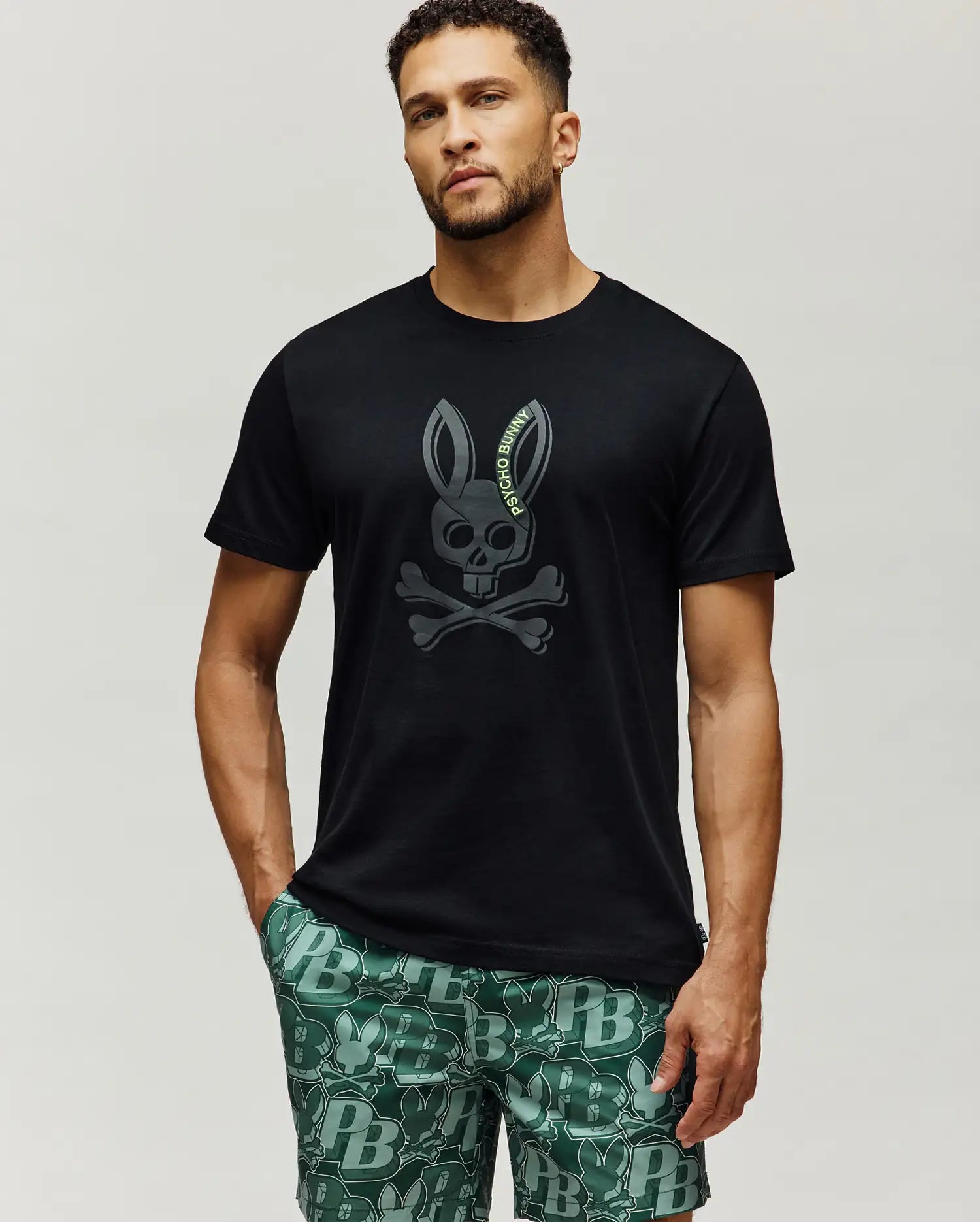 Mens Serge Embroidered Bunny Graphic Tee, black classic fit jersey knit with a large, centered dark grey embroidered Psycho Bunny skull and crossbones logo featuring lime green text.