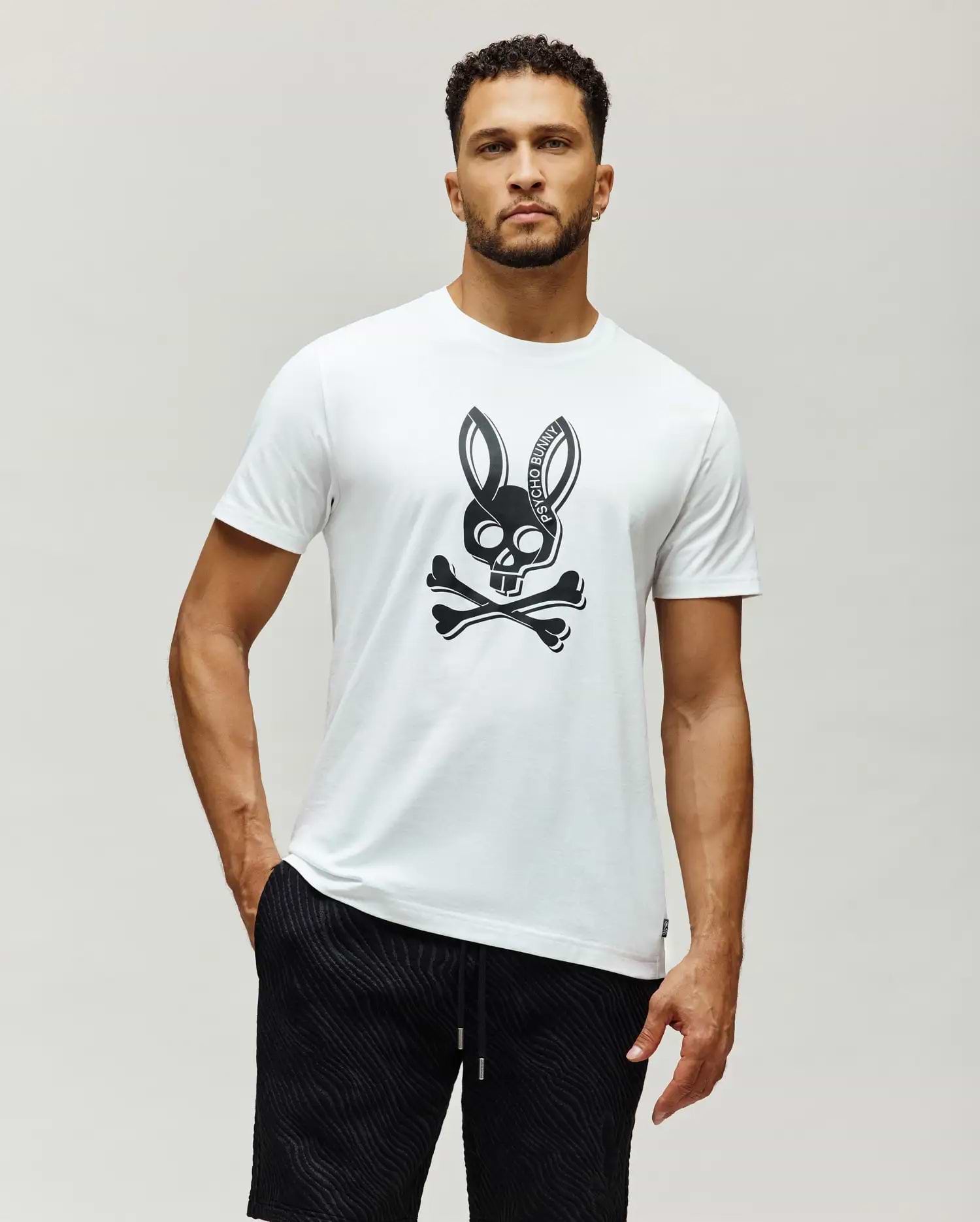 Mens Serge Embroidered Bunny Graphic Tee, a white classic fit jersey t-shirt featuring a large black Psycho Bunny skull and crossbones graphic centered on the chest.