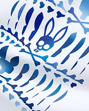 Mens Lewis Graphic Tee in white jersey fabric, showcasing a bold all-over gradient blue Psycho Bunny skull, crossbones, and stylized rib cage pattern for a refined streetwear look.