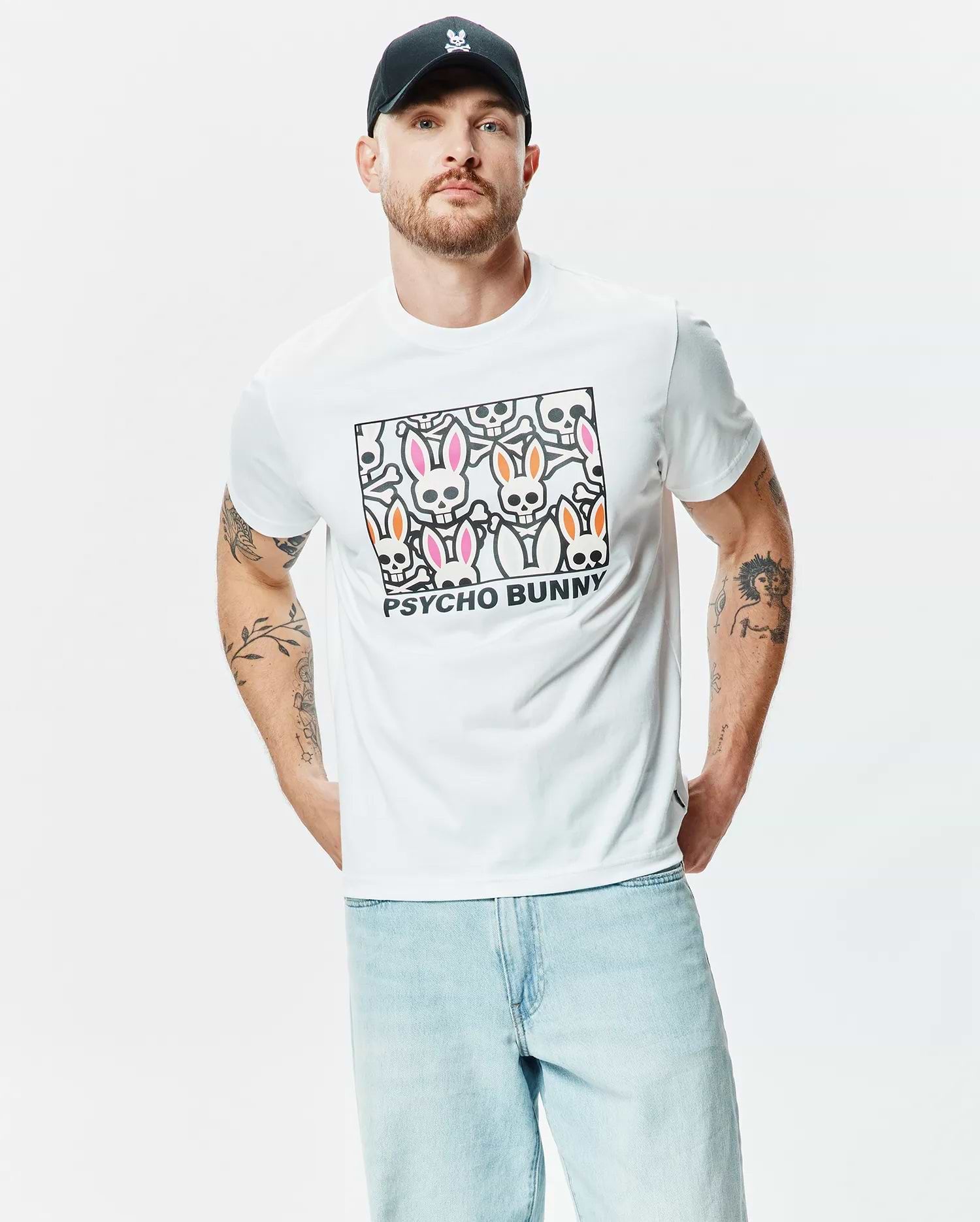 White Mens Byron Graphic Tee, a classic fit jersey t-shirt with a bold chest graphic featuring stylized pink and orange ear bunny skulls, bones, and black Psycho Bunny text. (2)
