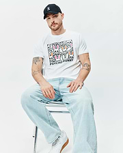 White Mens Byron Graphic Tee with a large central graphic print of colorful Psycho Bunny skull logos and PSYCHO BUNNY text, paired with a black cap featuring a small pink embroidered Psycho Bunny logo. (4)
