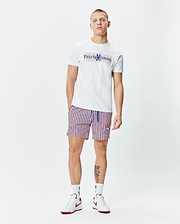 White Mens John Back Graphic Tee with a large layered blue and red Psycho Bunny text and skull logo on the chest, paired with white, red, and blue striped shorts featuring a small embroidered bunny skull logo on the left leg.