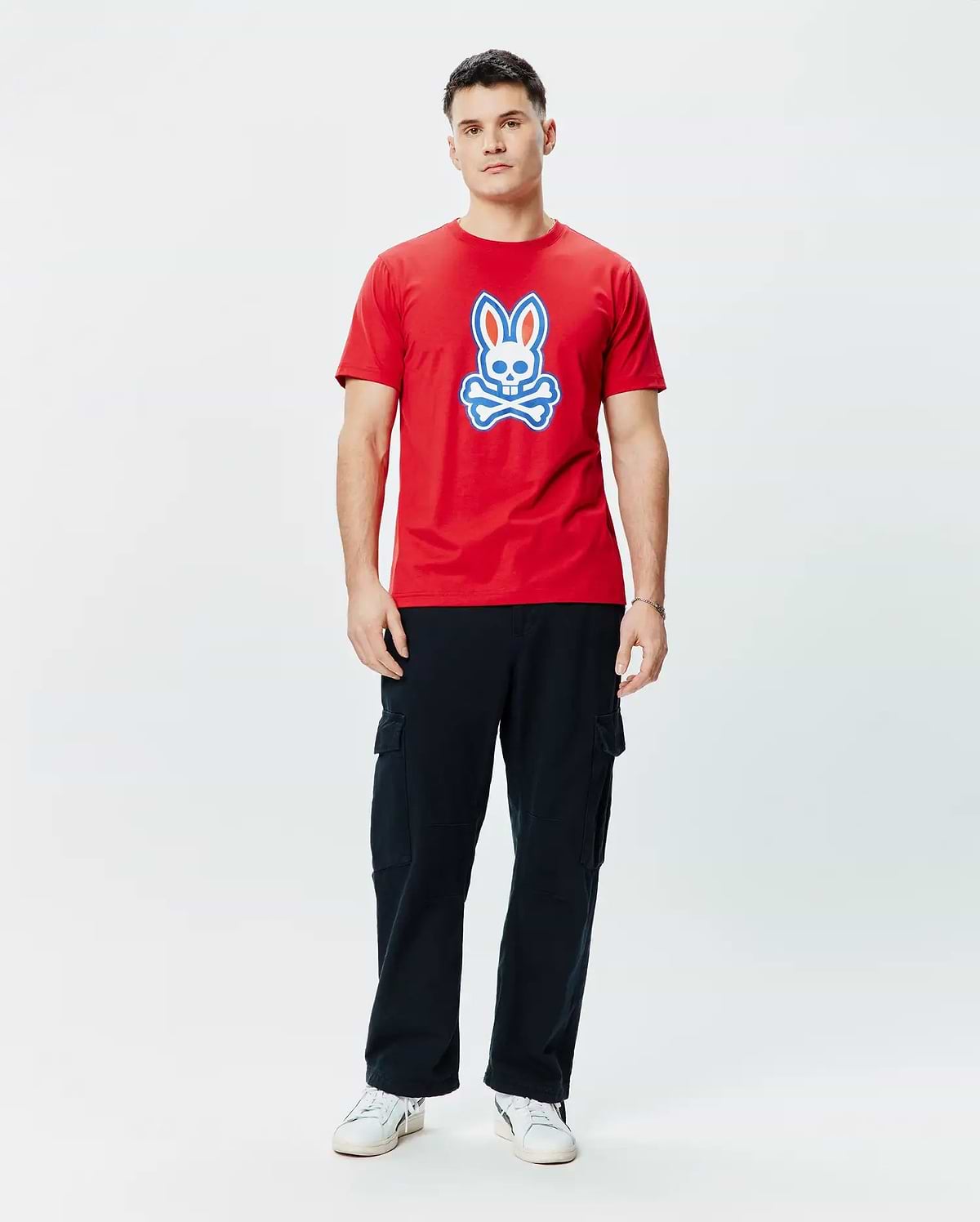 Mens John Graphic Tee. Vibrant red classic fit jersey t-shirt featuring a prominent, centered Psycho Bunny skull logo graphic in white and blue, embodying refined streetwear style.