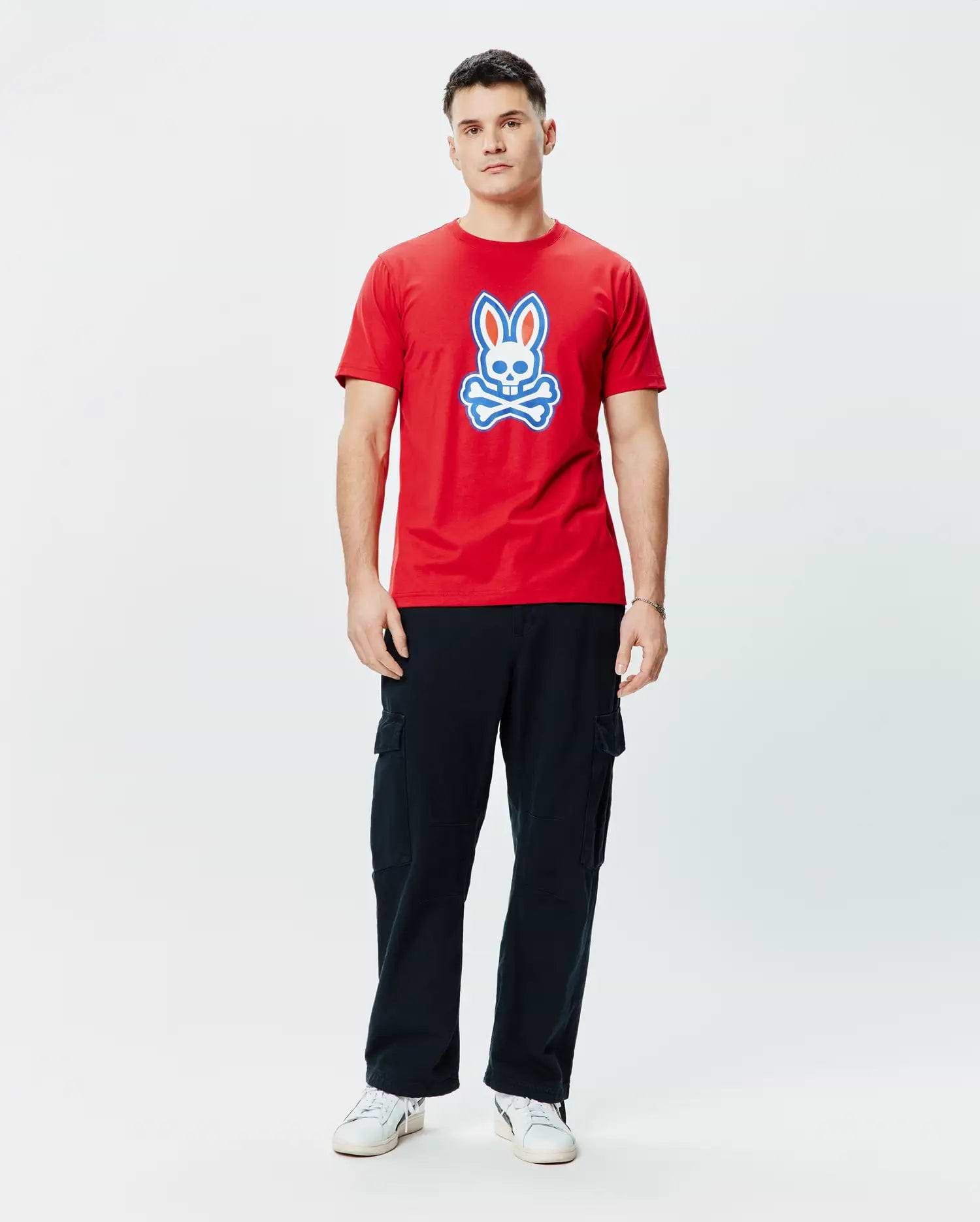 Mens John Graphic Tee. Vibrant red classic fit jersey t-shirt featuring a prominent, centered Psycho Bunny skull logo graphic in white and blue, embodying refined streetwear style.