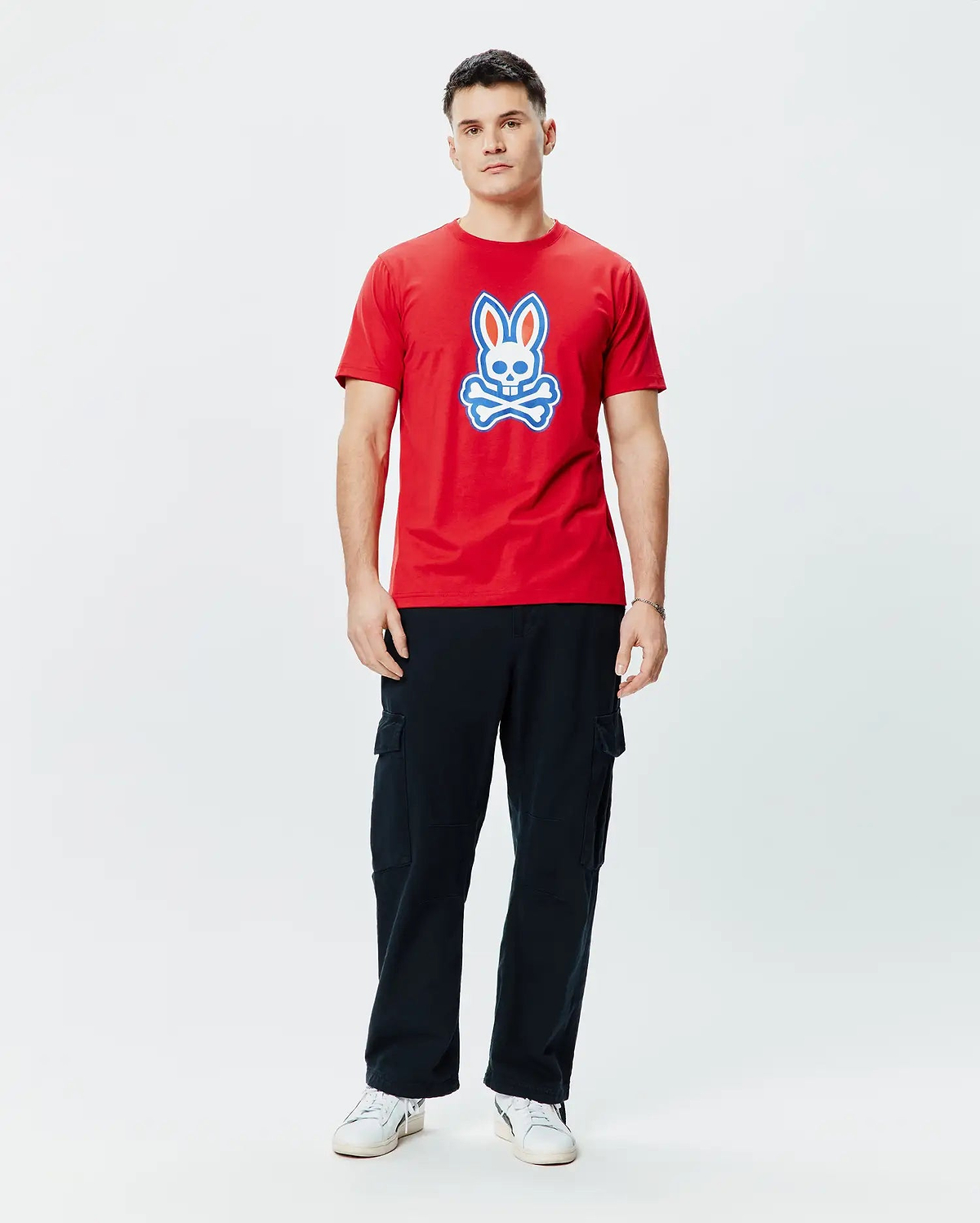 Mens John Graphic Tee. Vibrant red classic fit jersey t-shirt featuring a prominent, centered Psycho Bunny skull logo graphic in white and blue, embodying refined streetwear style.