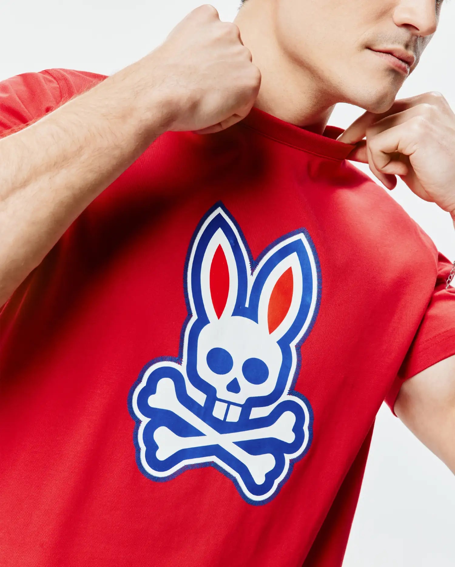 Mens John Graphic Tee, a classic fit red jersey knit t-shirt featuring a large central graphic Psycho Bunny skull and crossbones logo in white, blue, and red.
