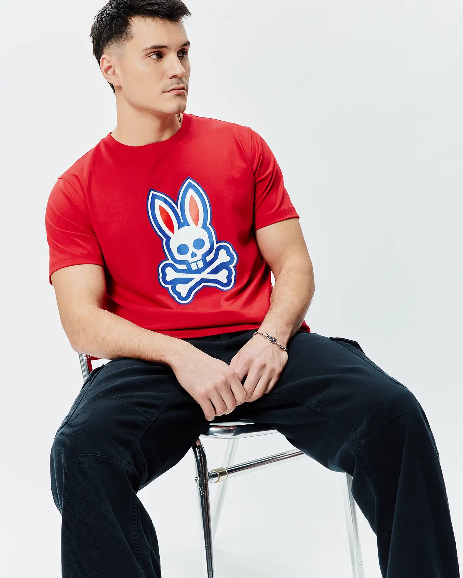 Mens John Graphic Tee, a classic fit red jersey t-shirt featuring a large white, blue, and red Psycho Bunny skull and crossbones graphic print on the center chest.