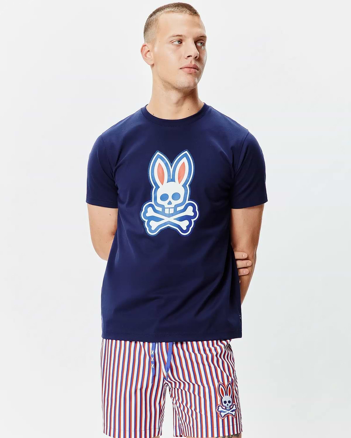 Mens John Graphic Tee, a classic fit navy blue jersey knit t-shirt featuring a large white, light blue, and orange Psycho Bunny skull graphic on the chest and a smaller one on the upper back.