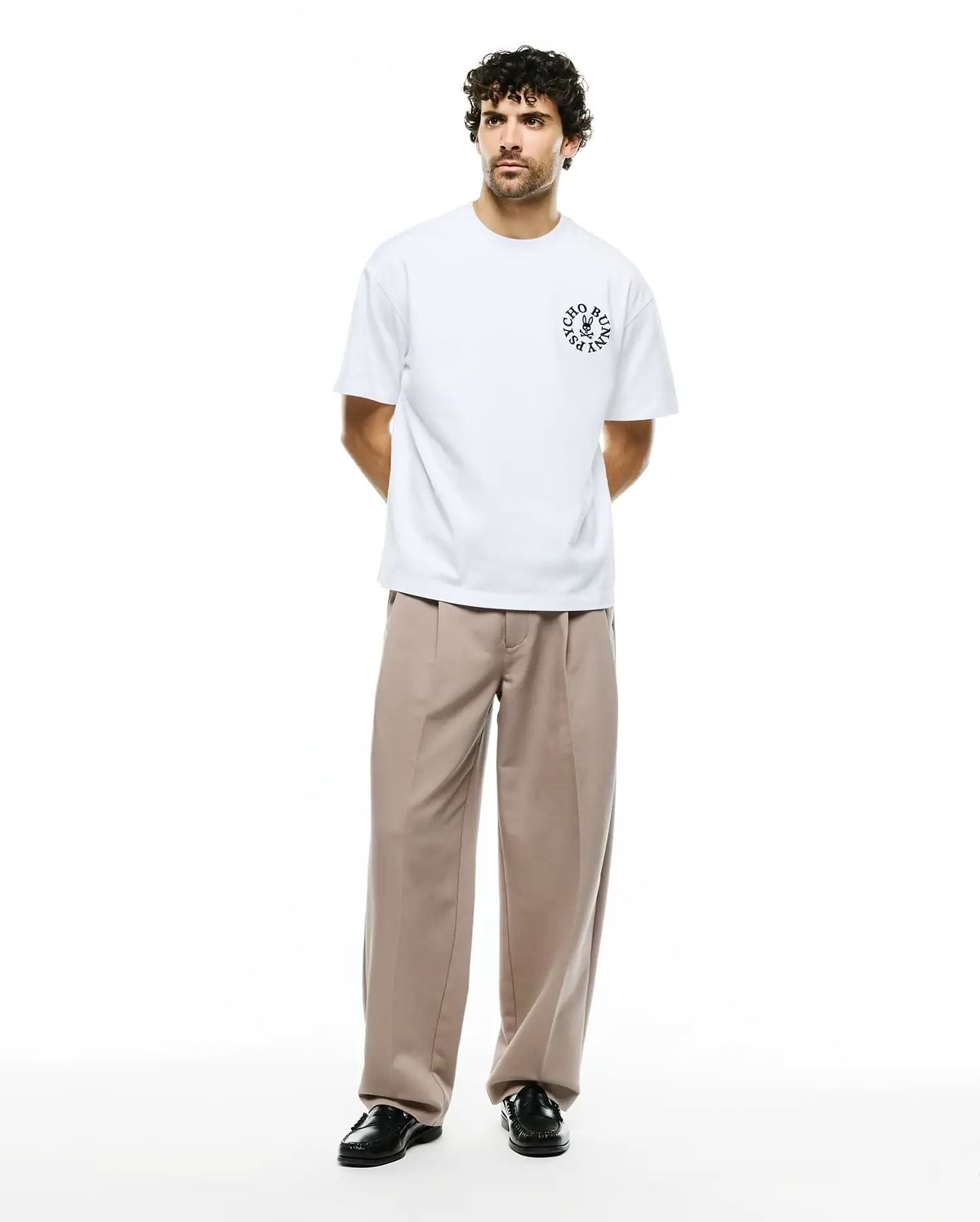 Mens Olek Relaxed Back Graphic Tee, a white relaxed-fit jersey t-shirt featuring a black circular Psycho Bunny skull logo with text on the left chest. (5)