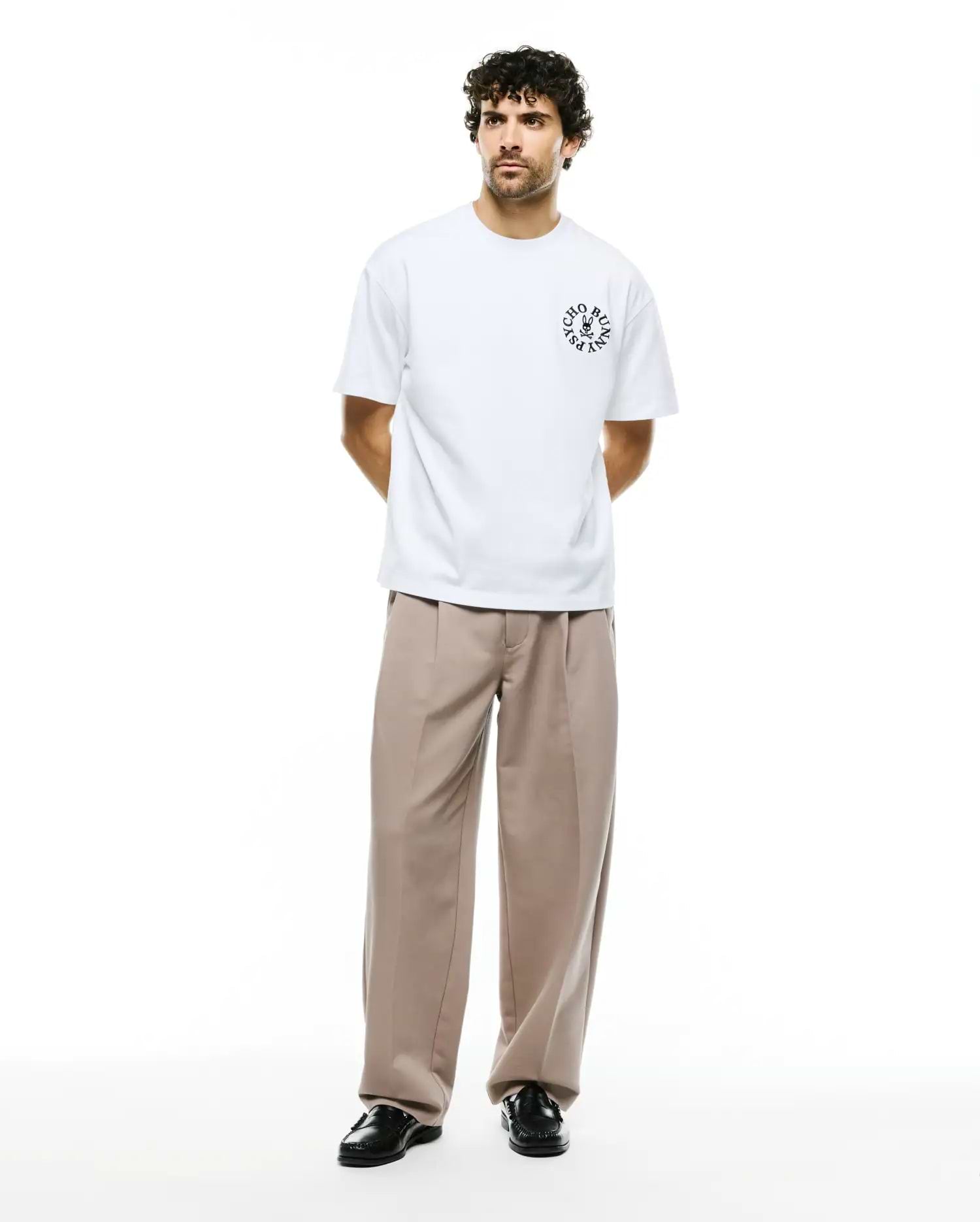 Mens Olek Relaxed Back Graphic Tee, a white relaxed-fit jersey t-shirt featuring a black circular Psycho Bunny skull logo with text on the left chest. (5)