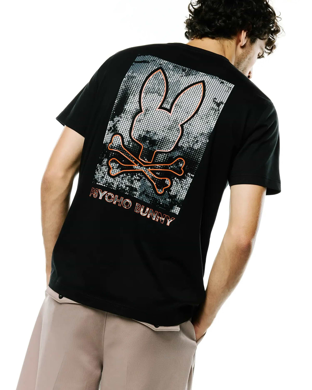 Black classic fit jersey t-shirt with a large back graphic featuring an orange outlined Psycho Bunny skull and crossbones over a grey pixelated background, with PSYCHO BUNNY text below. Men's Alfie Back Graphic Tee. (1)