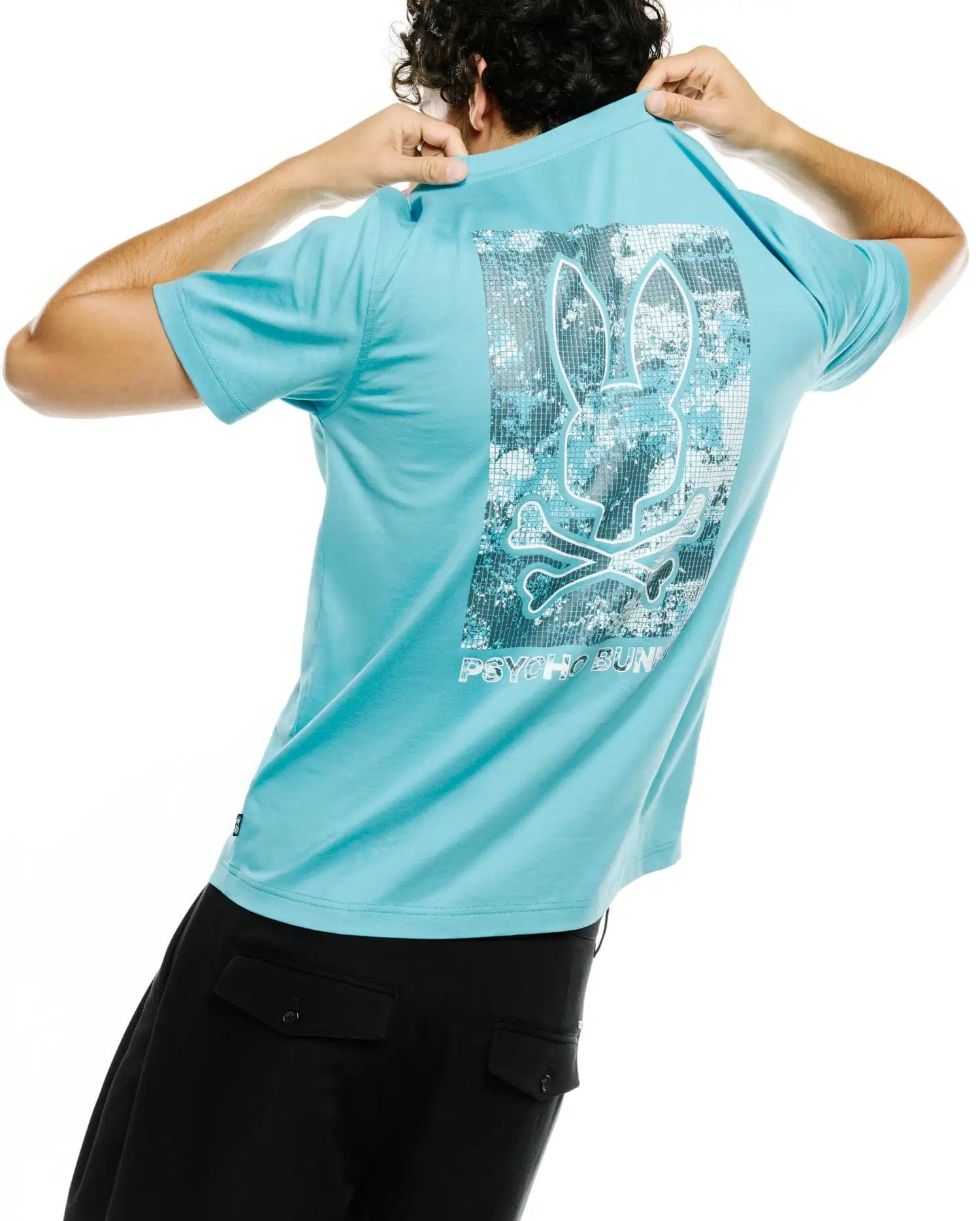 Men's Alfie Back Graphic Tee, a classic fit aqua blue jersey t-shirt with a large back graphic featuring a white-outlined Psycho Bunny skull over a pixelated silver digital camo pattern and PSYCHO BUNNY text. (1)