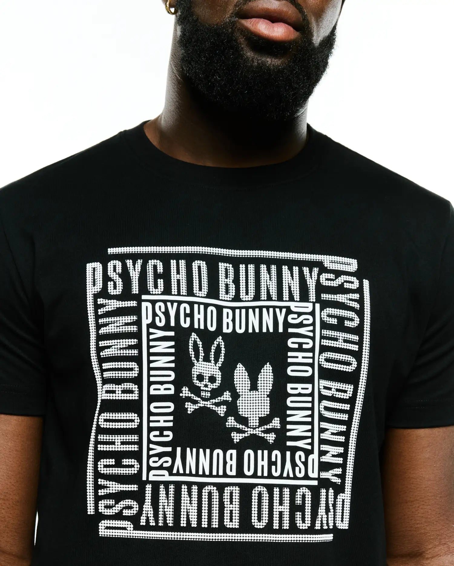Men's Raj Wordmark Graphic Tee, a black classic fit jersey t-shirt featuring a large white dotted graphic of the Psycho Bunny wordmark repeated in a square frame with two bunny skull logos and crossbones on the chest. (3)