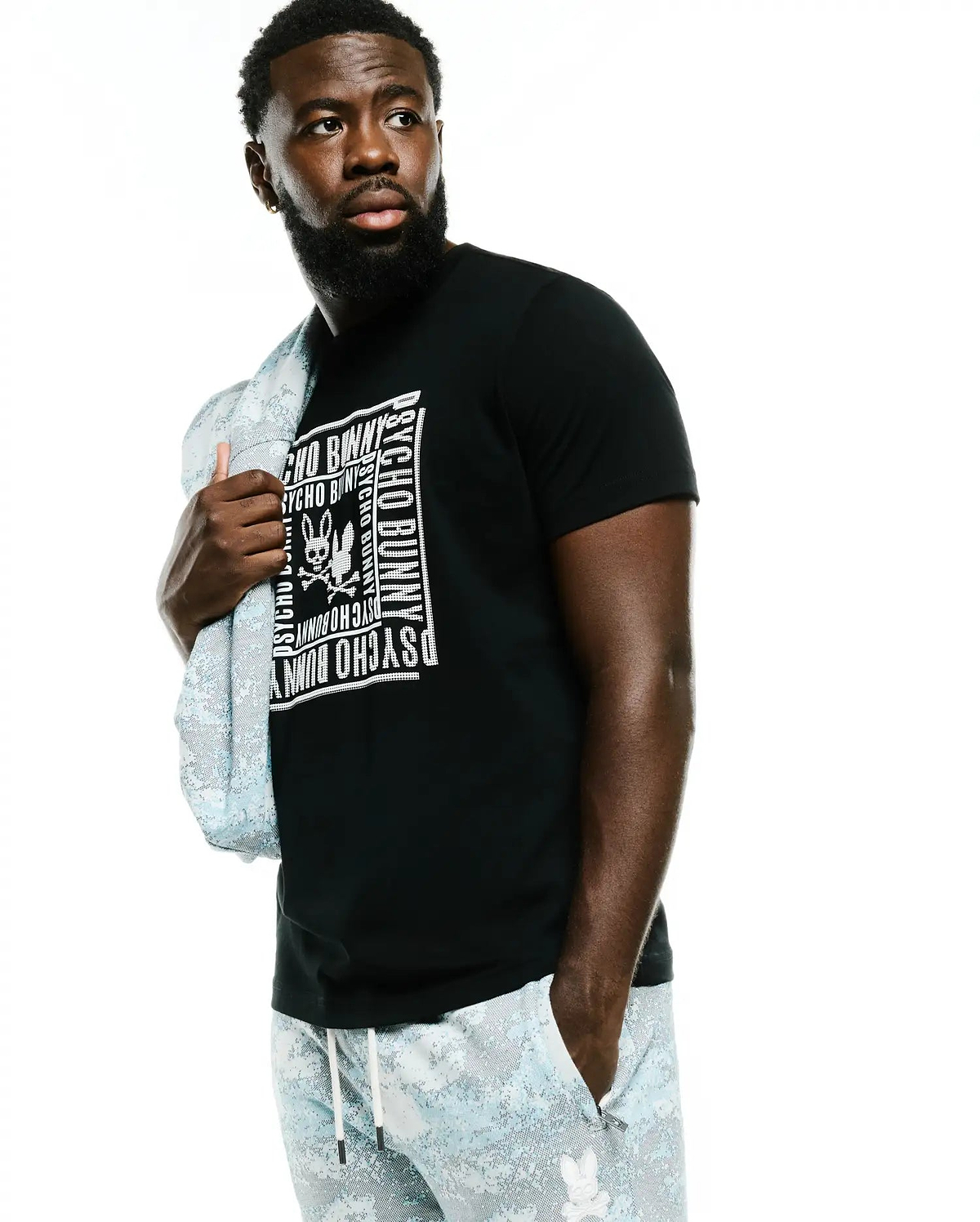 Men's Raj Wordmark Graphic Tee, a black classic-fit jersey t-shirt with a large white central chest graphic featuring the Psycho Bunny skull logo and repeated wordmark. (4)