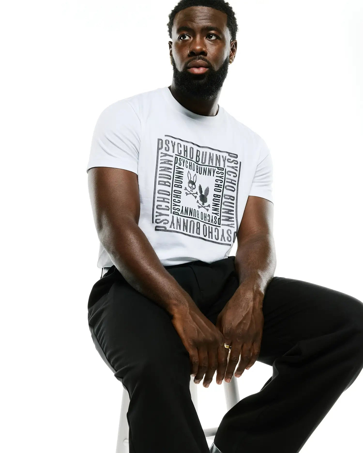 Men's Raj Wordmark Graphic Tee, a white classic fit jersey t-shirt featuring a large black chest graphic with repeated dotted Psycho Bunny wordmark framing the iconic bunny skull logo. (4)