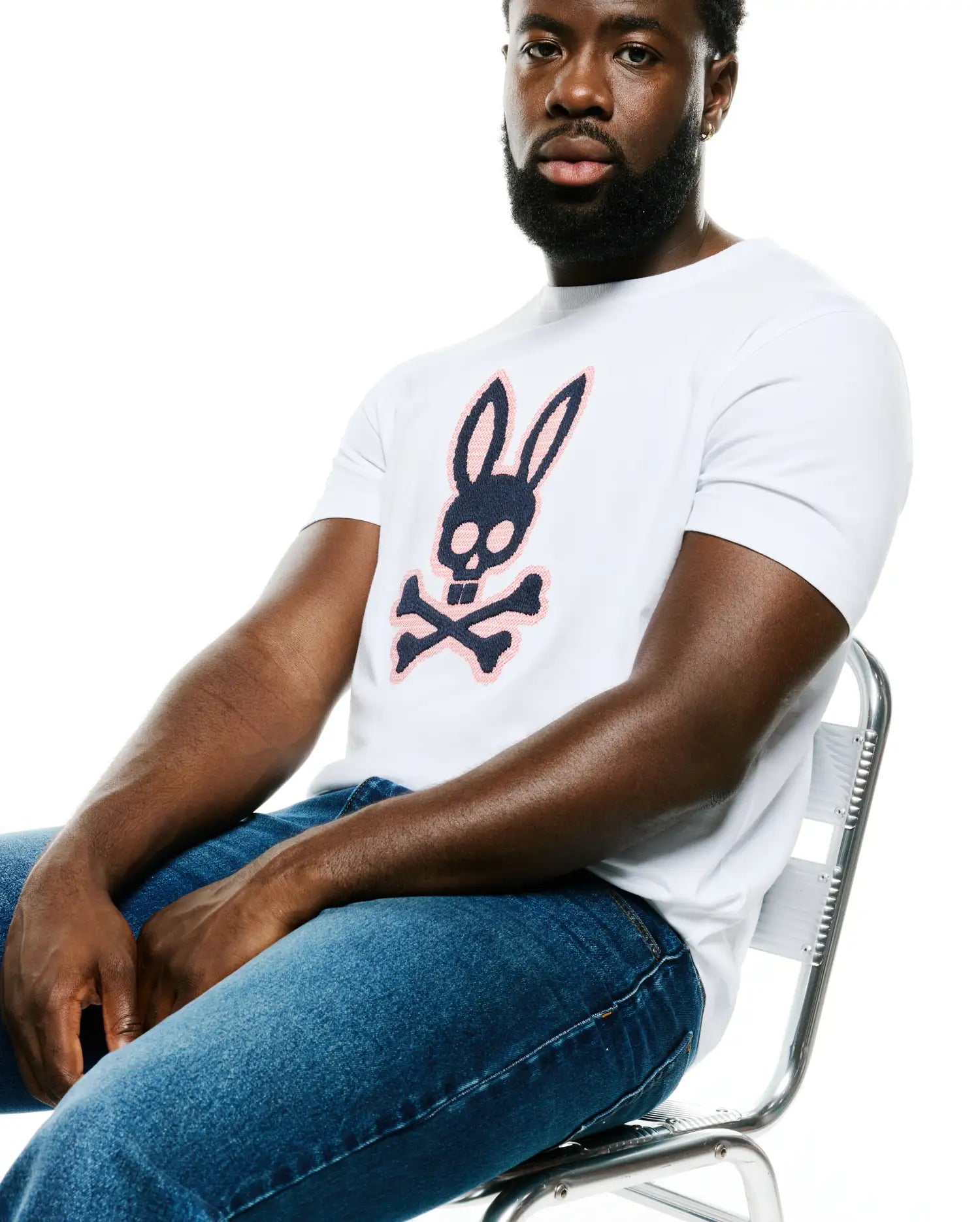 Men's Samson Graphic Tee, a premium white classic fit soft cotton jersey t-shirt featuring a bold central navy and blush pink Psycho Bunny skull and crossbones graphic logo, embodying refined streetwear. (4)