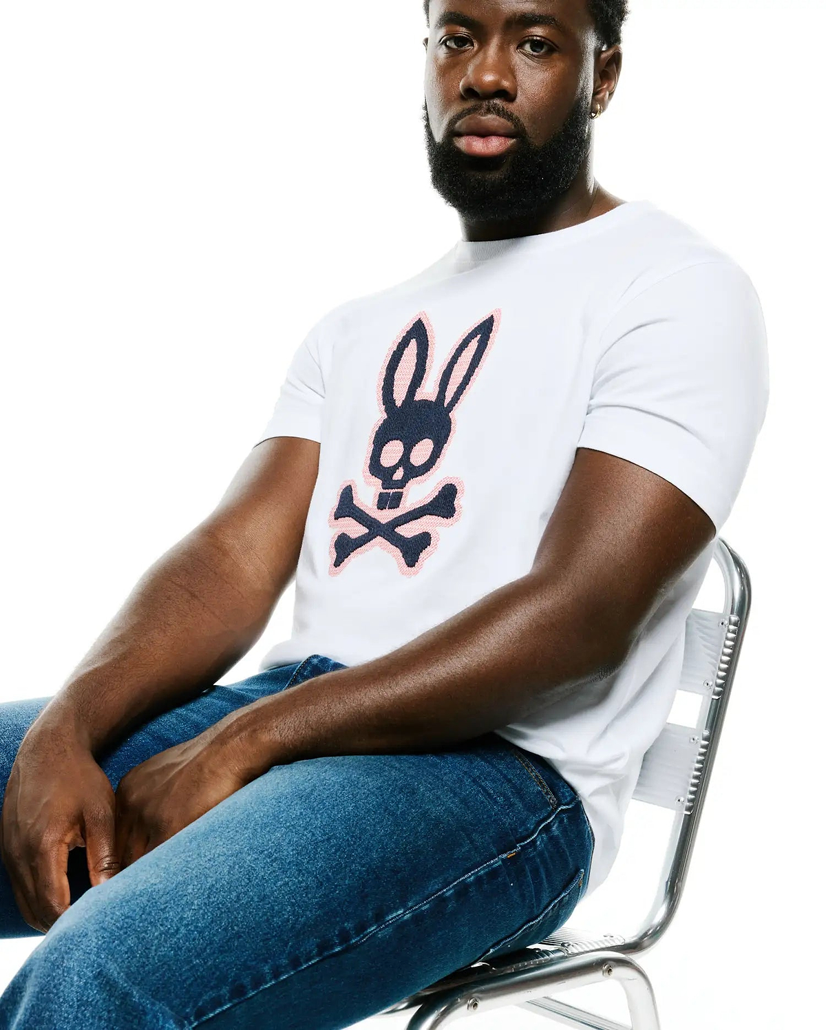 Men's Samson Graphic Tee, a premium white classic fit soft cotton jersey t-shirt featuring a bold central navy and blush pink Psycho Bunny skull and crossbones graphic logo, embodying refined streetwear. (4)