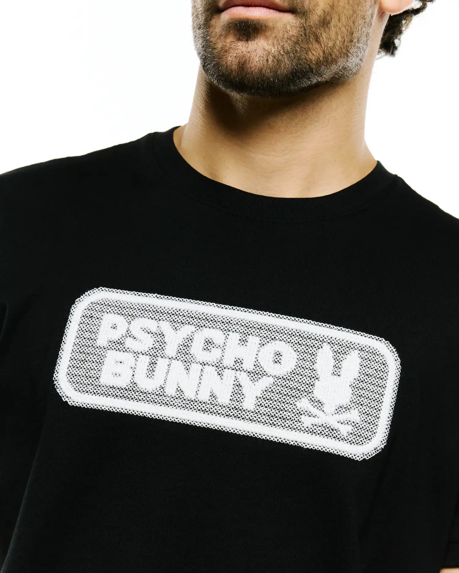 Black classic fit jersey T-shirt featuring a prominent white textured mesh graphic of the Psycho Bunny wordmark and iconic bunny skull logo on the chest. Men's Samson Wordmark Graphic Tee. (3)