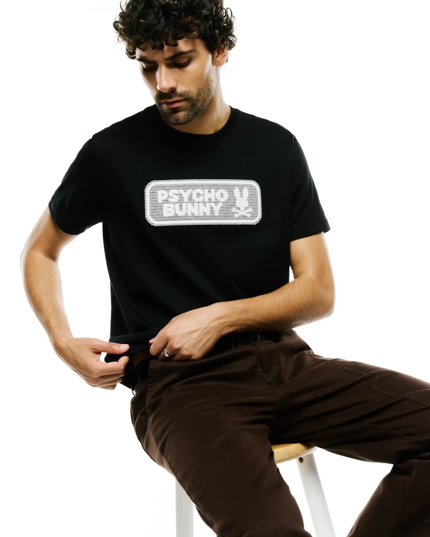 Black classic fit jersey t-shirt, the Men's Samson Wordmark Graphic Tee, features a large, centered white rectangular graphic with a textured Psycho Bunny wordmark and iconic skull logo. (4)